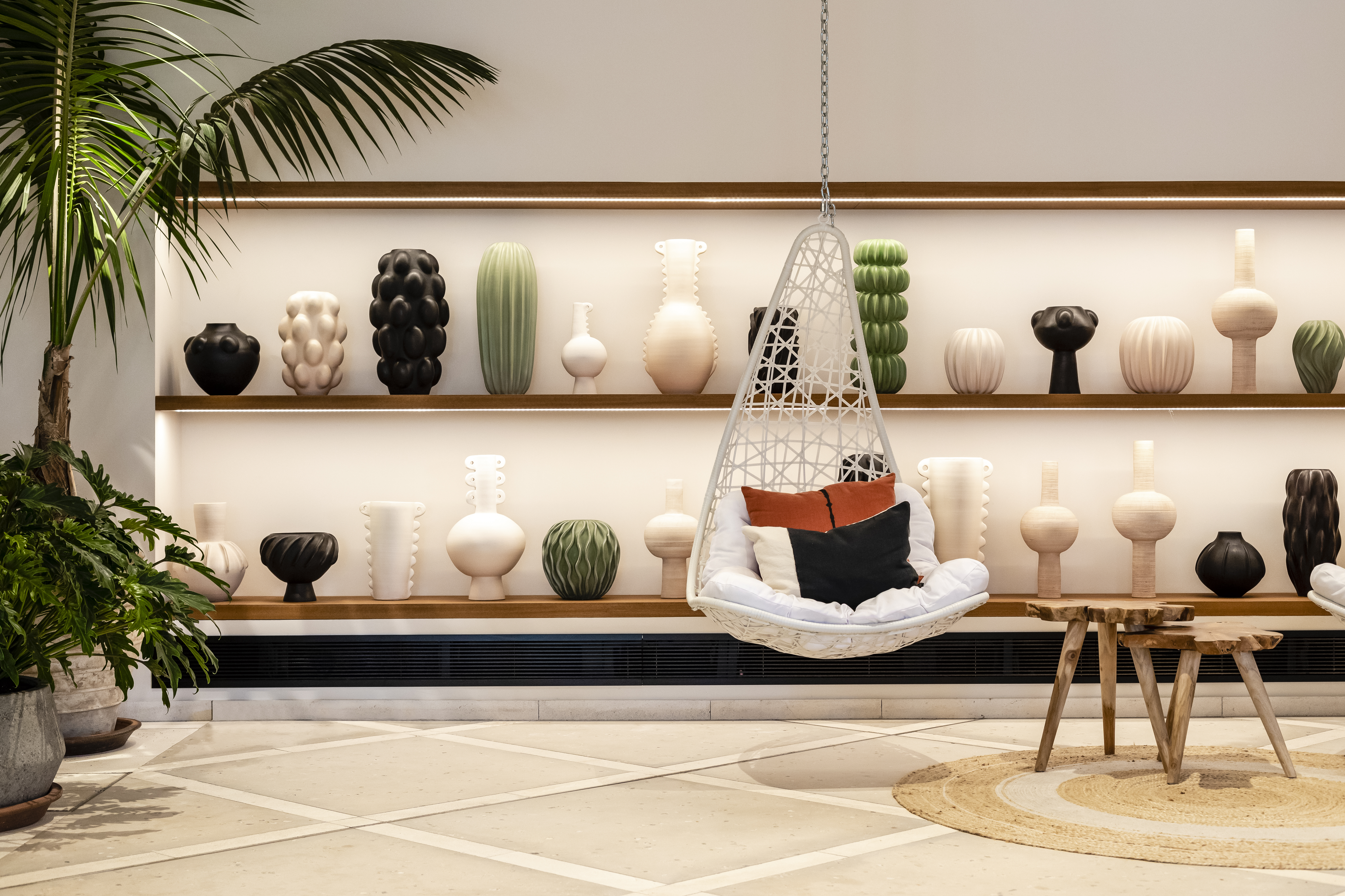 An indoor space featuring a variety of decorative vases on shelving, a hanging chair with cushions, and a potted palm tree