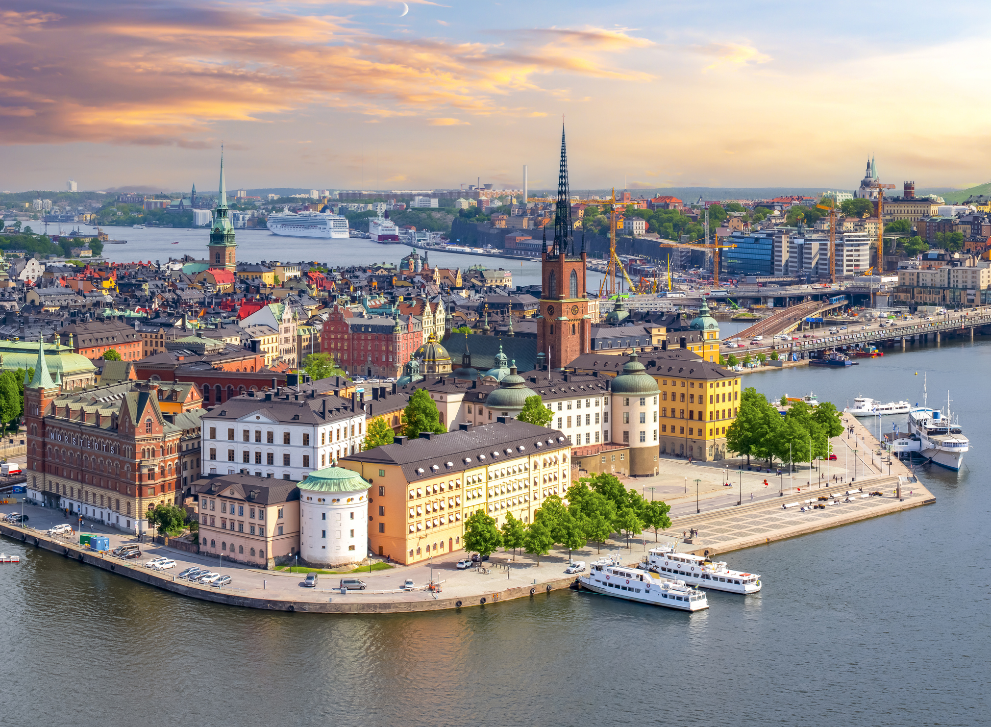 Aerial view of Stockholm cityscape with historic buildings, waterways, and boats during sunset.