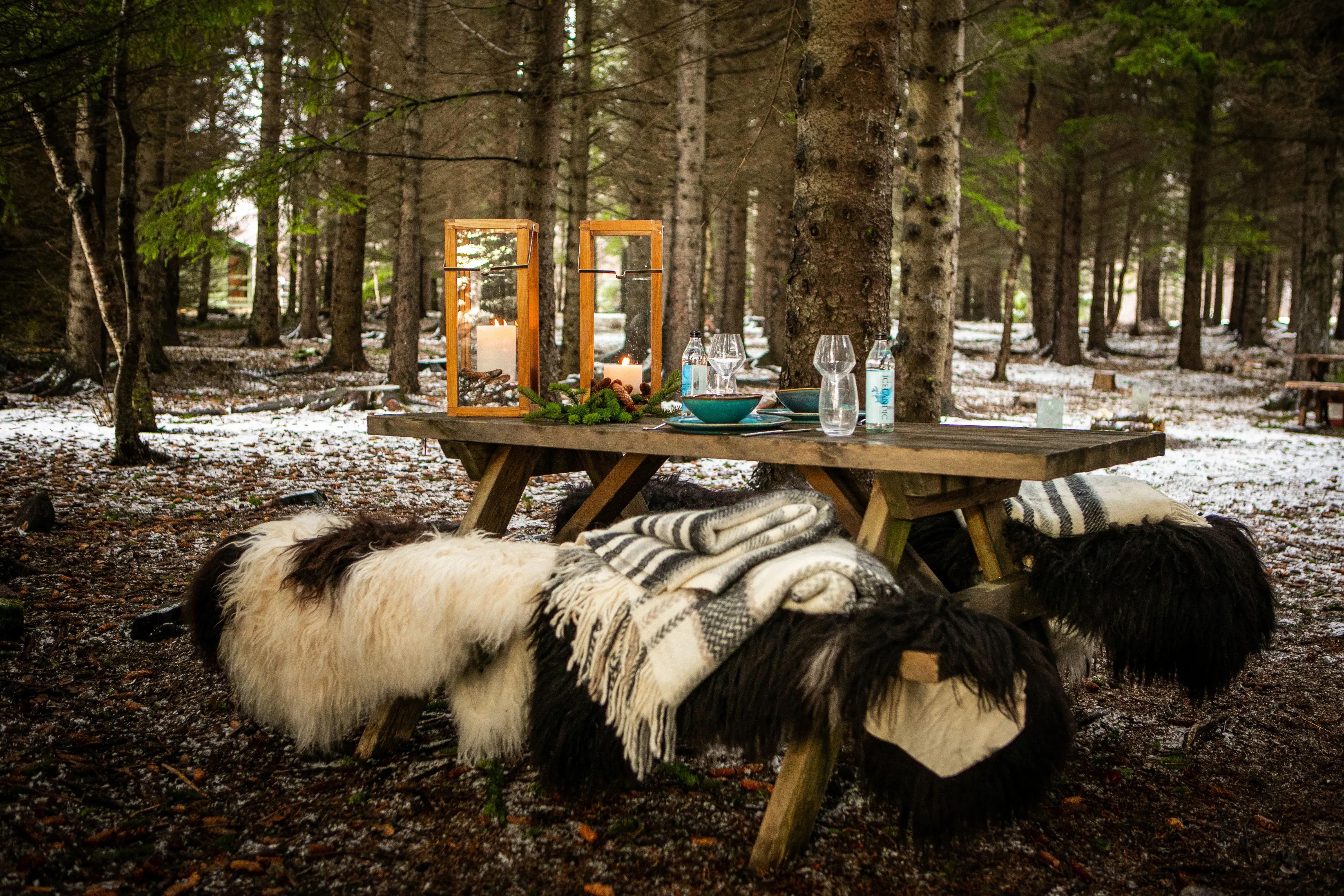 A cosy outdoor dining set up with blankets in the middle of the forest