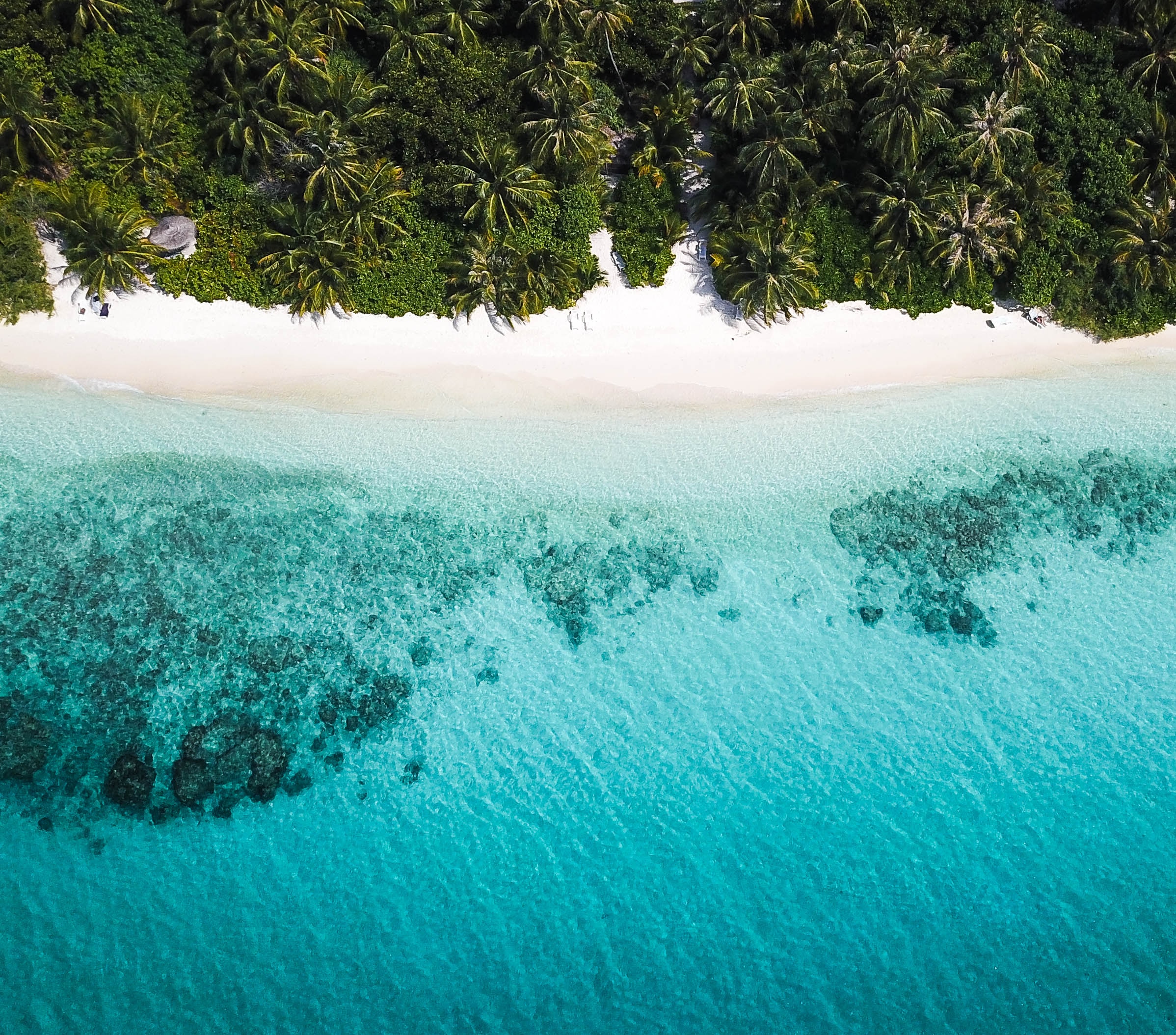 An aerial view of blue clear sea water by a white sandy beach