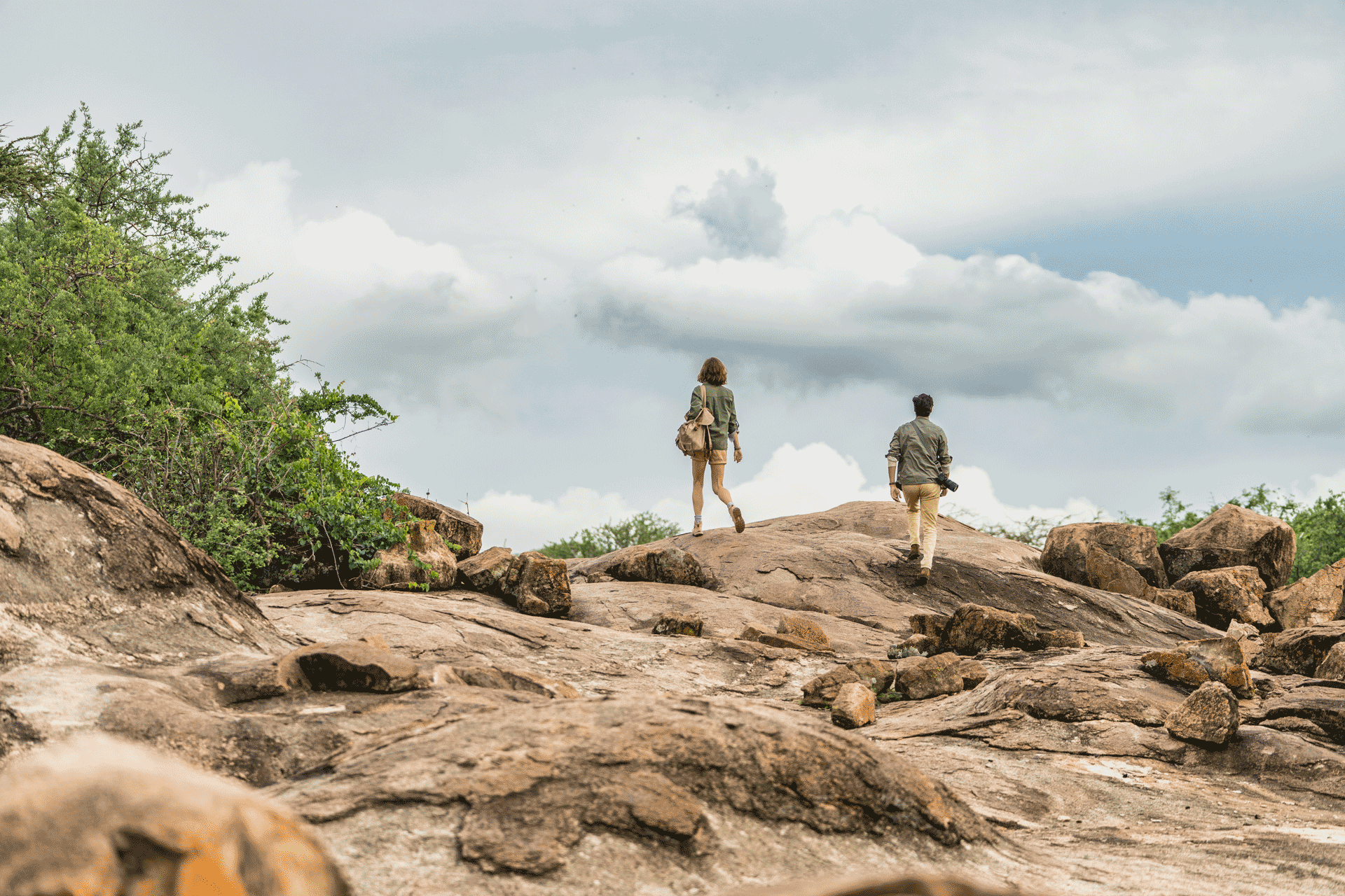 Two guests walking across rugged rocky terrain during a guided nature walk in a remote wilderness setting.