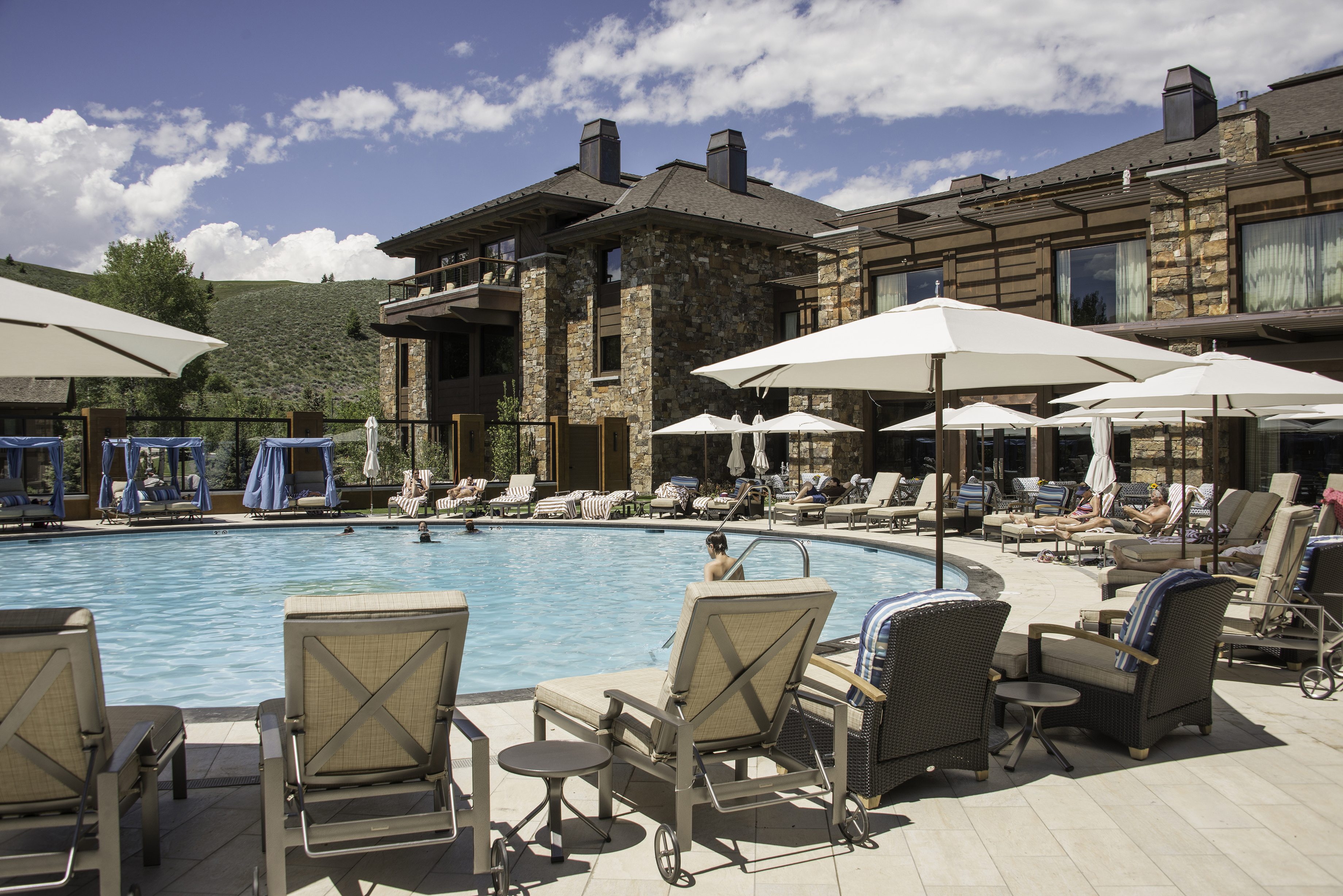 Outdoor pool area at Sun Valley Lodge with lounge chairs, umbrellas, and people relaxing by the water on a sunny day