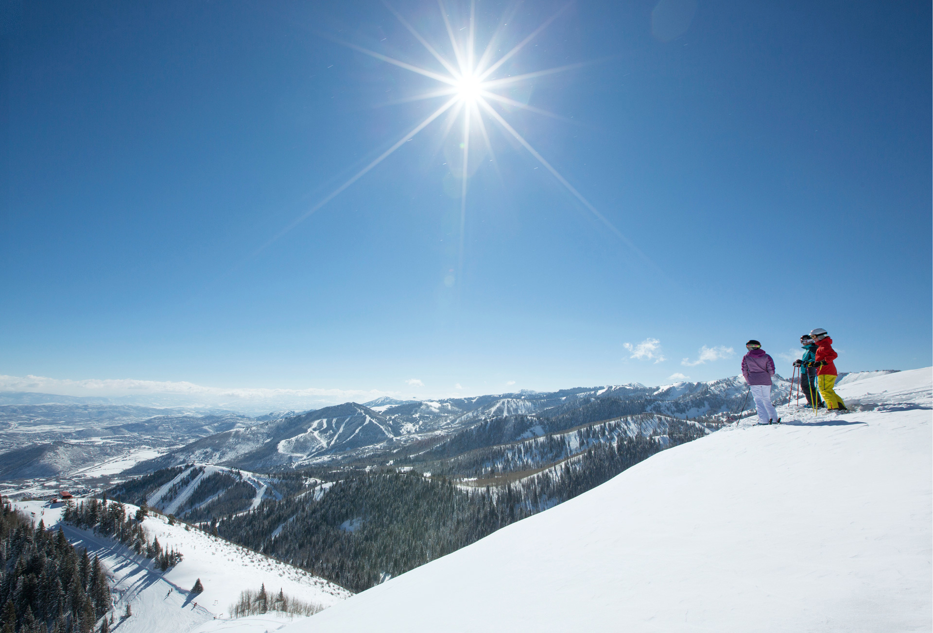 Three skiers stopped to look over the mountainous landscape from a snow covered peak