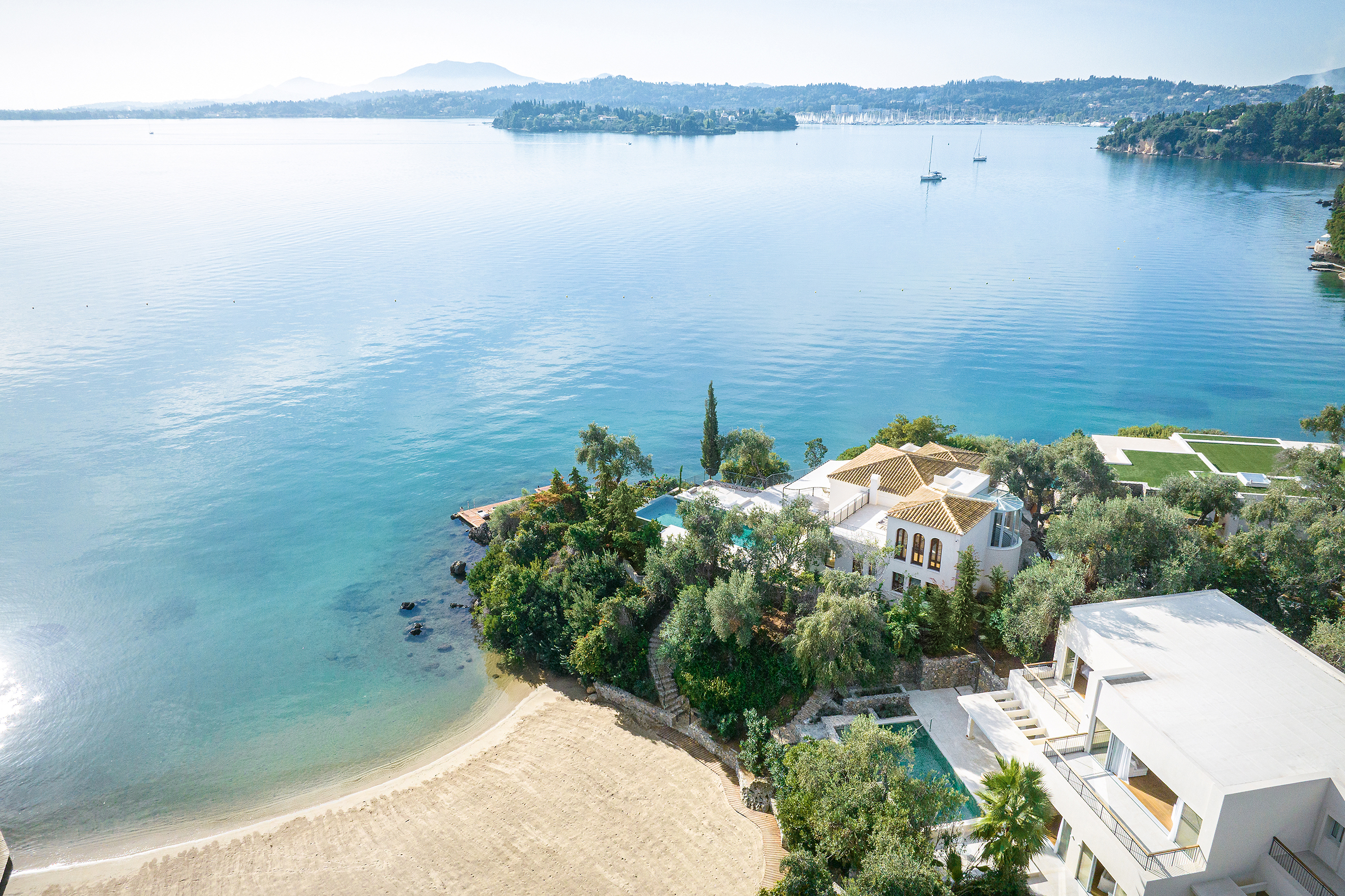Aerial view of Grecotel Corfu Imperial featuring luxury villas, private pools, and a sandy beach on the Ionian coast.