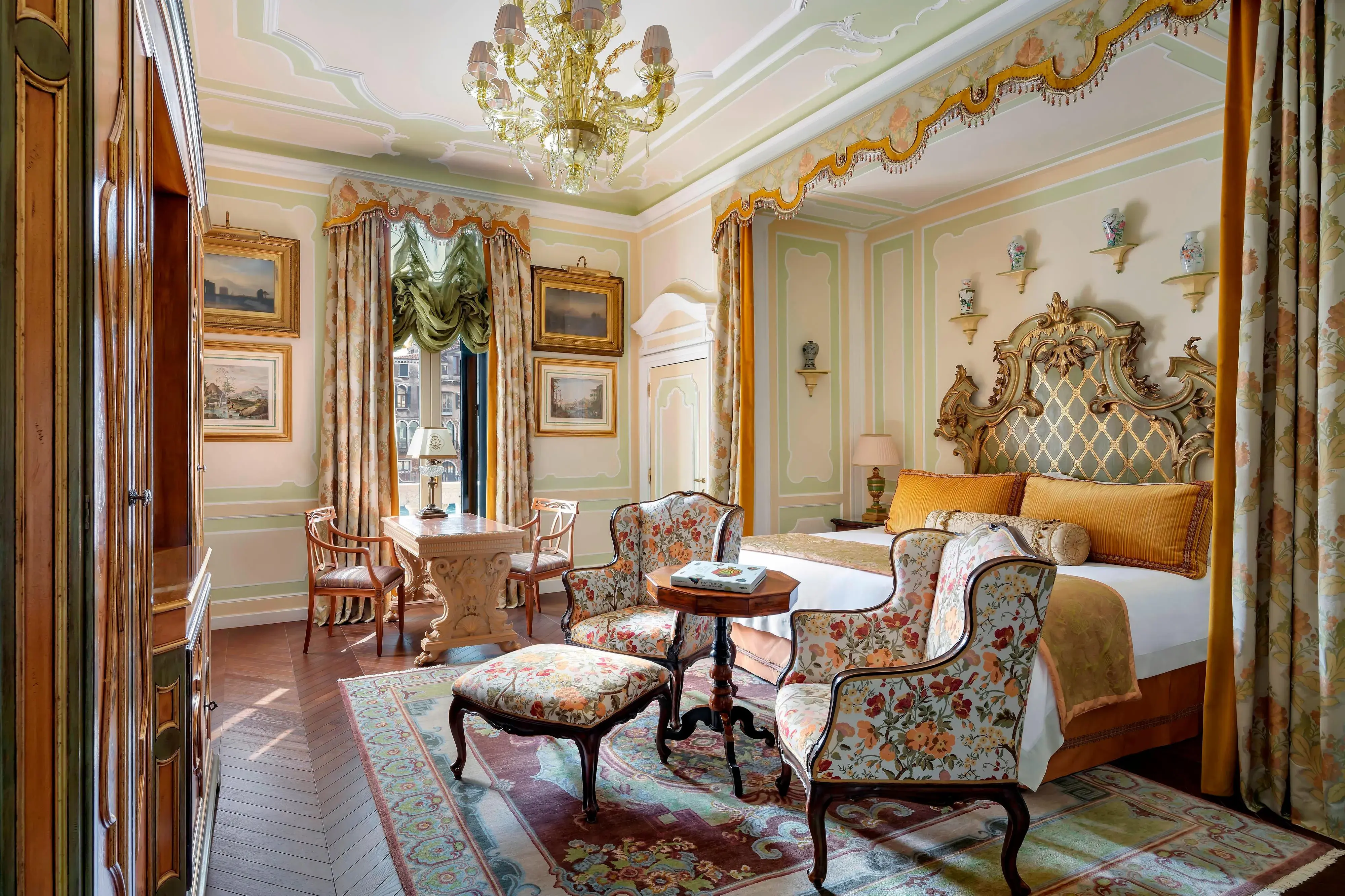 Elegant bedroom at The Gritti Palace in Venice with ornate headboard, floral armchairs, and classic Venetian décor.