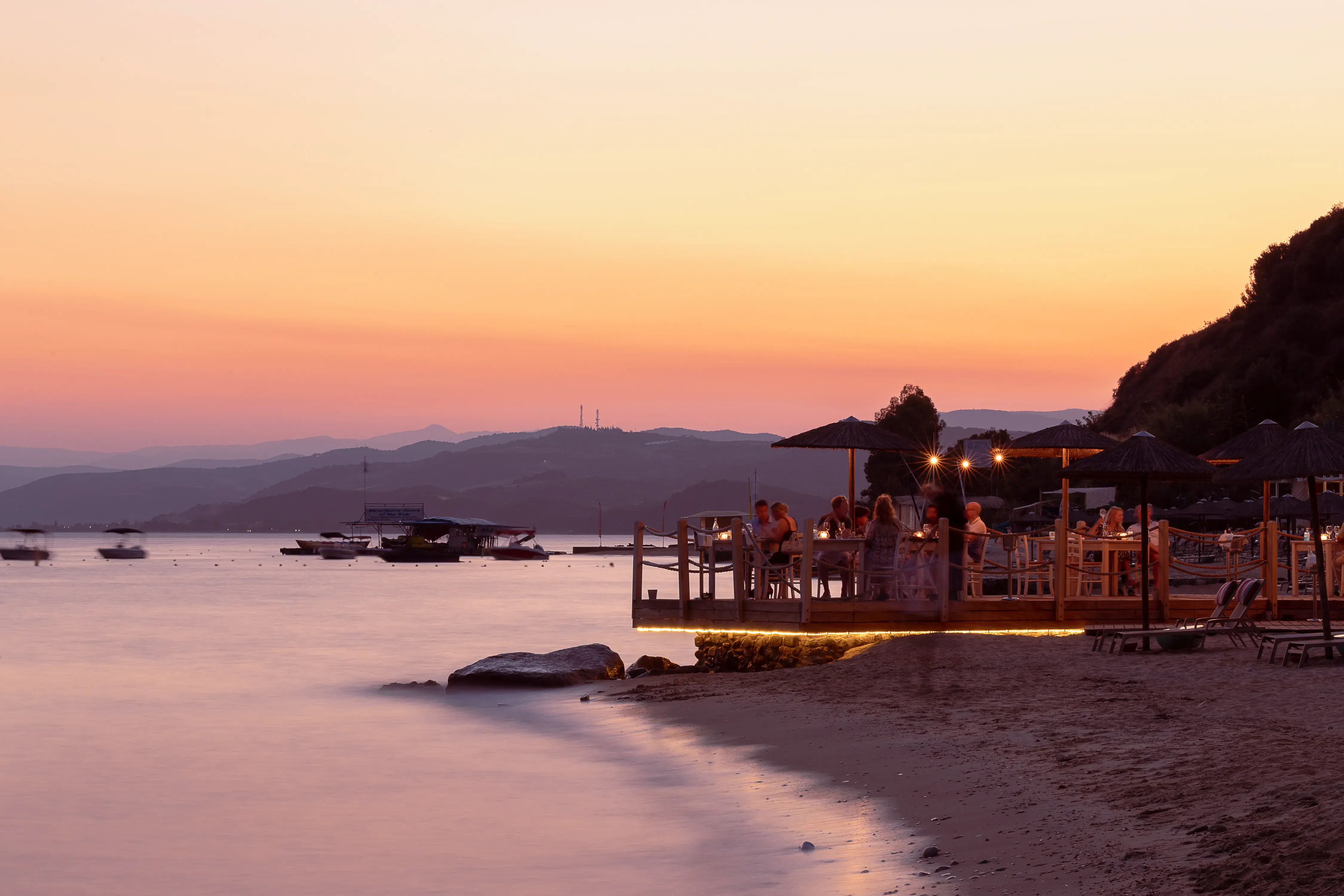 Sunset beachside dining at Eagles Palace in Greece with soft golden light, calm waves and guests enjoying the waterfront atmosphere.