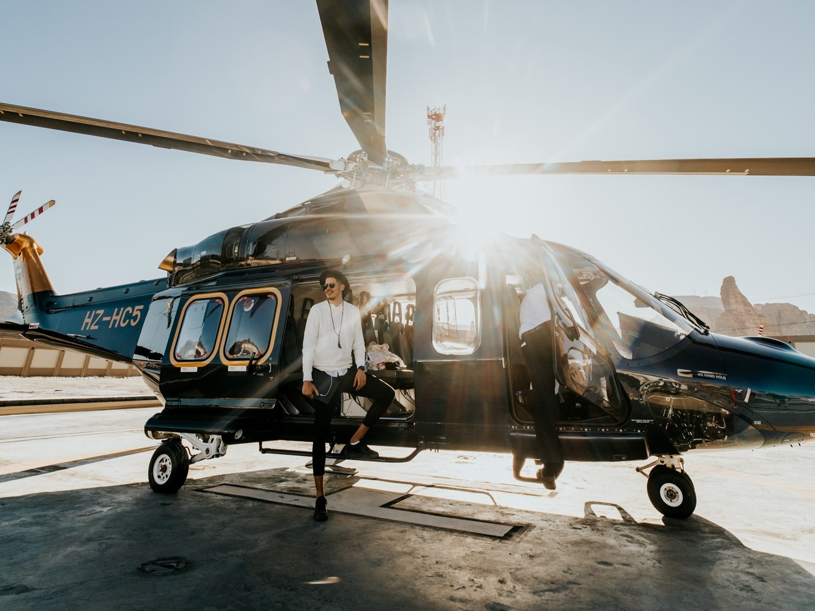 Person standing beside a black helicopter under bright sunlight