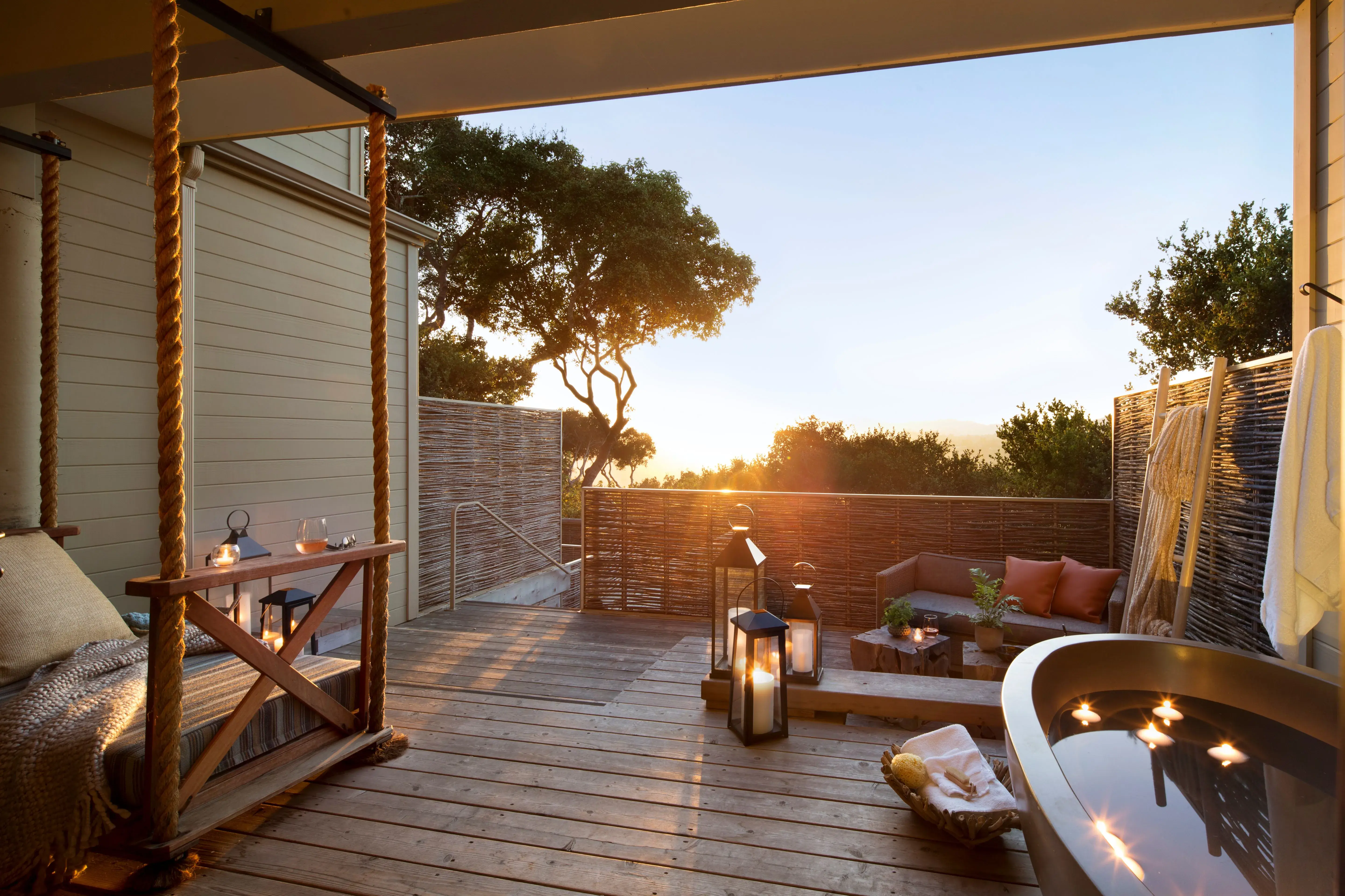 The terrace of a Vineyard Oak Studio at Carmel Valley Ranch in California, featuring a deep bath tub,  lounge cabana and candles with the sunset behind
