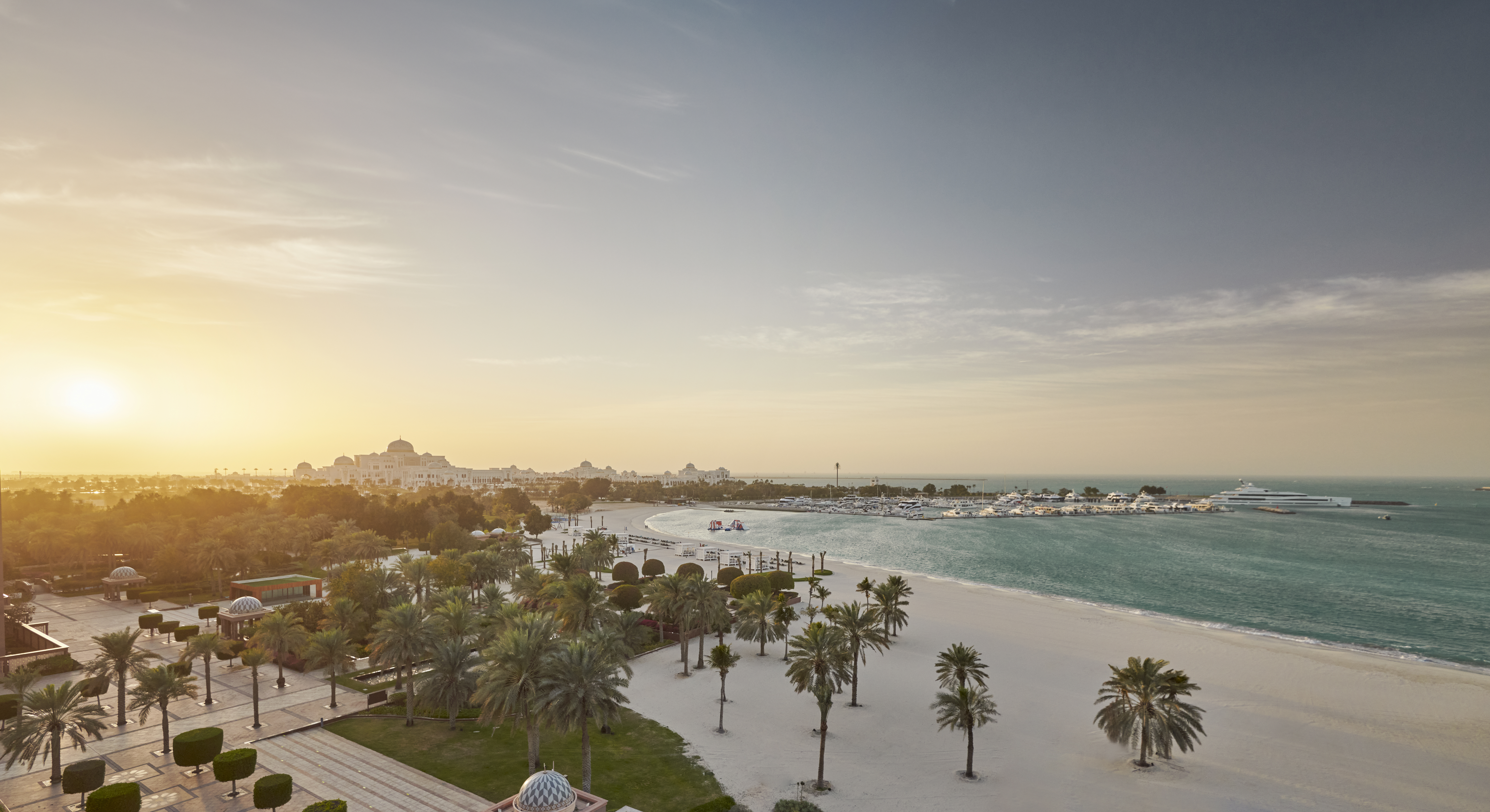 A sandy beach dappled with palms with a marina and large building beyond at Emirates Palace Mandarin Oriental, Abu Dhabi