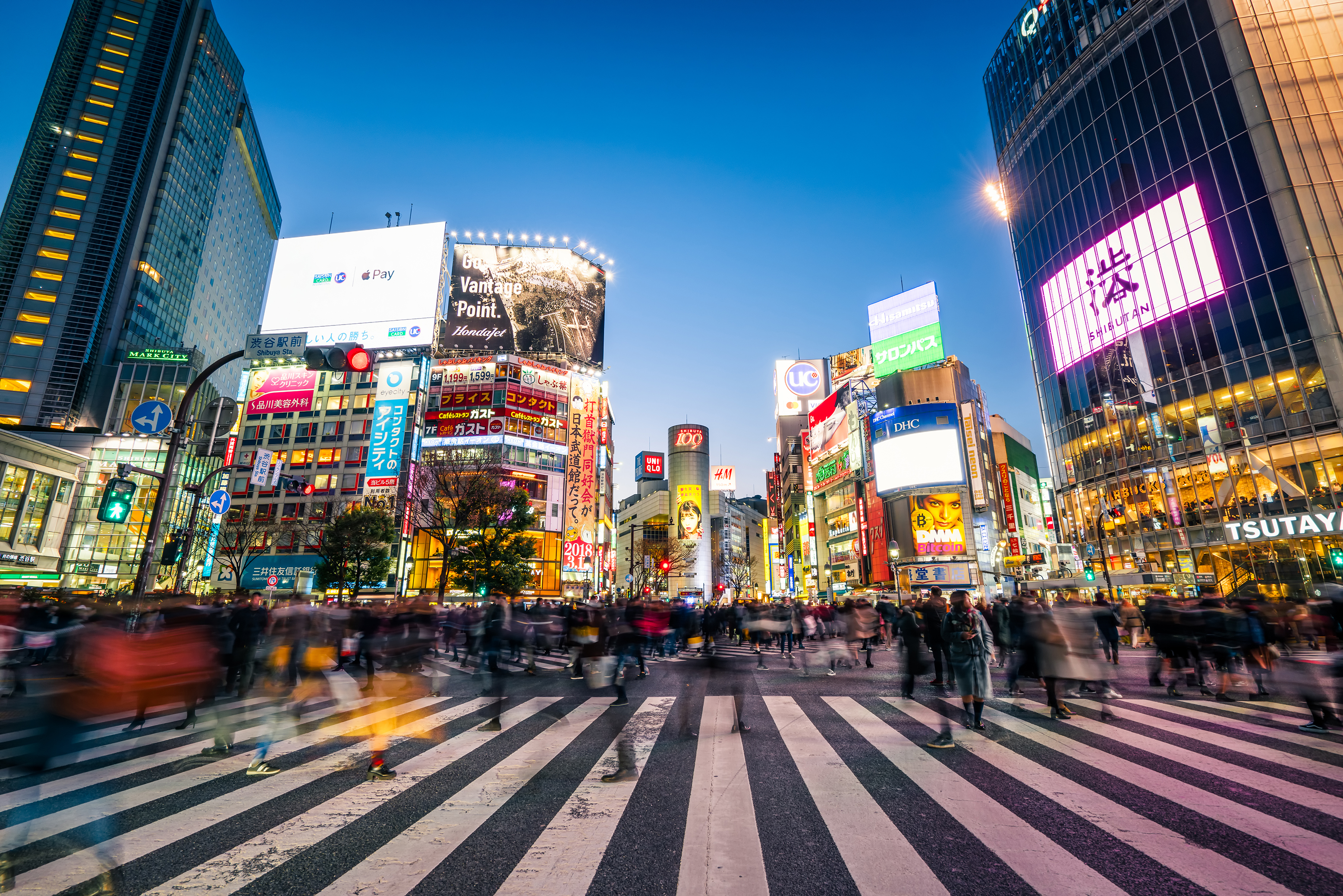 Tokyo's scramble crossing during dusk with people crossing and large buildings lit up