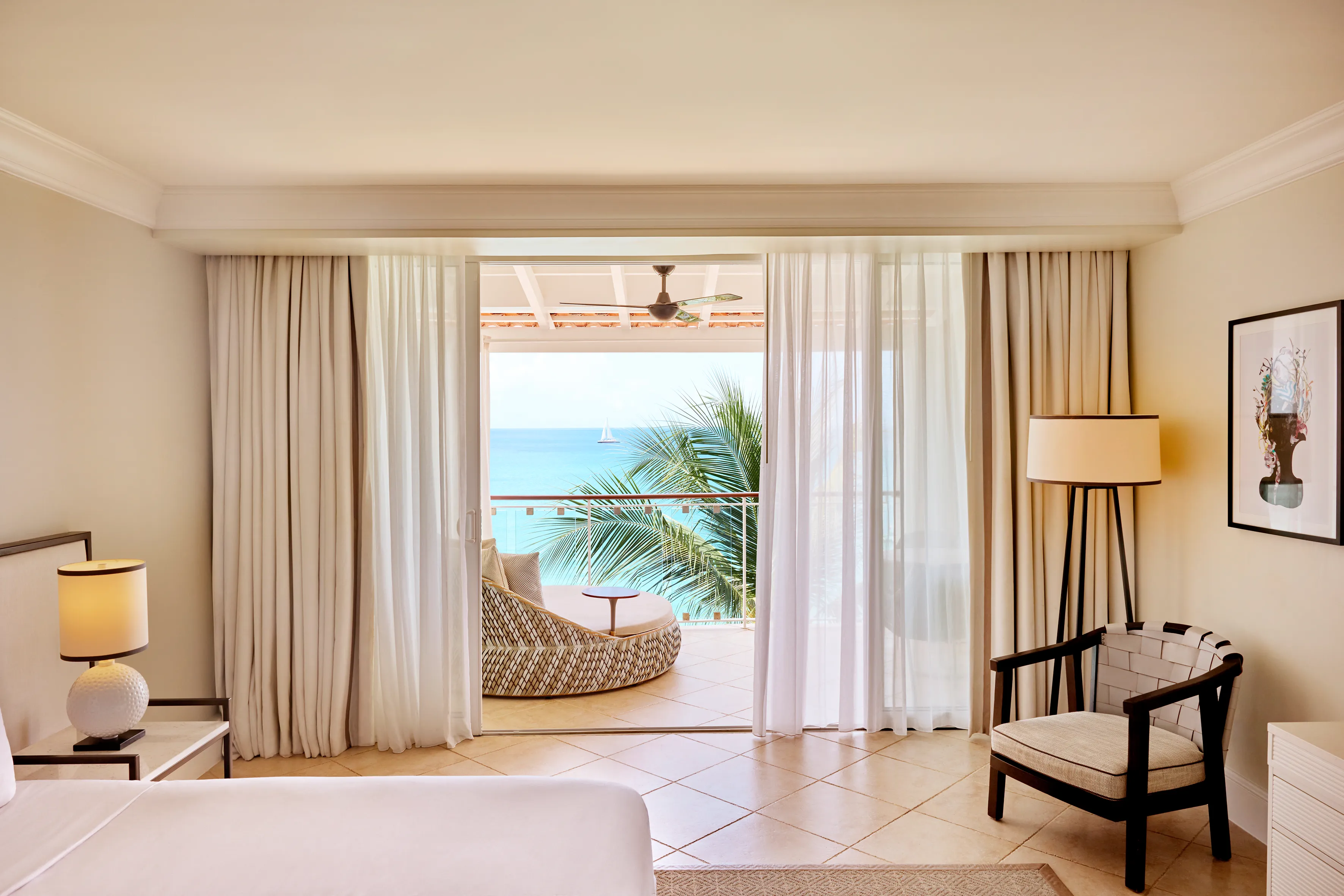An airy Signature Oceanfront Suite at Fairmont Royal Pavilion in Barbados featuring chic decor, a terrace and views of the ocean past palm trees