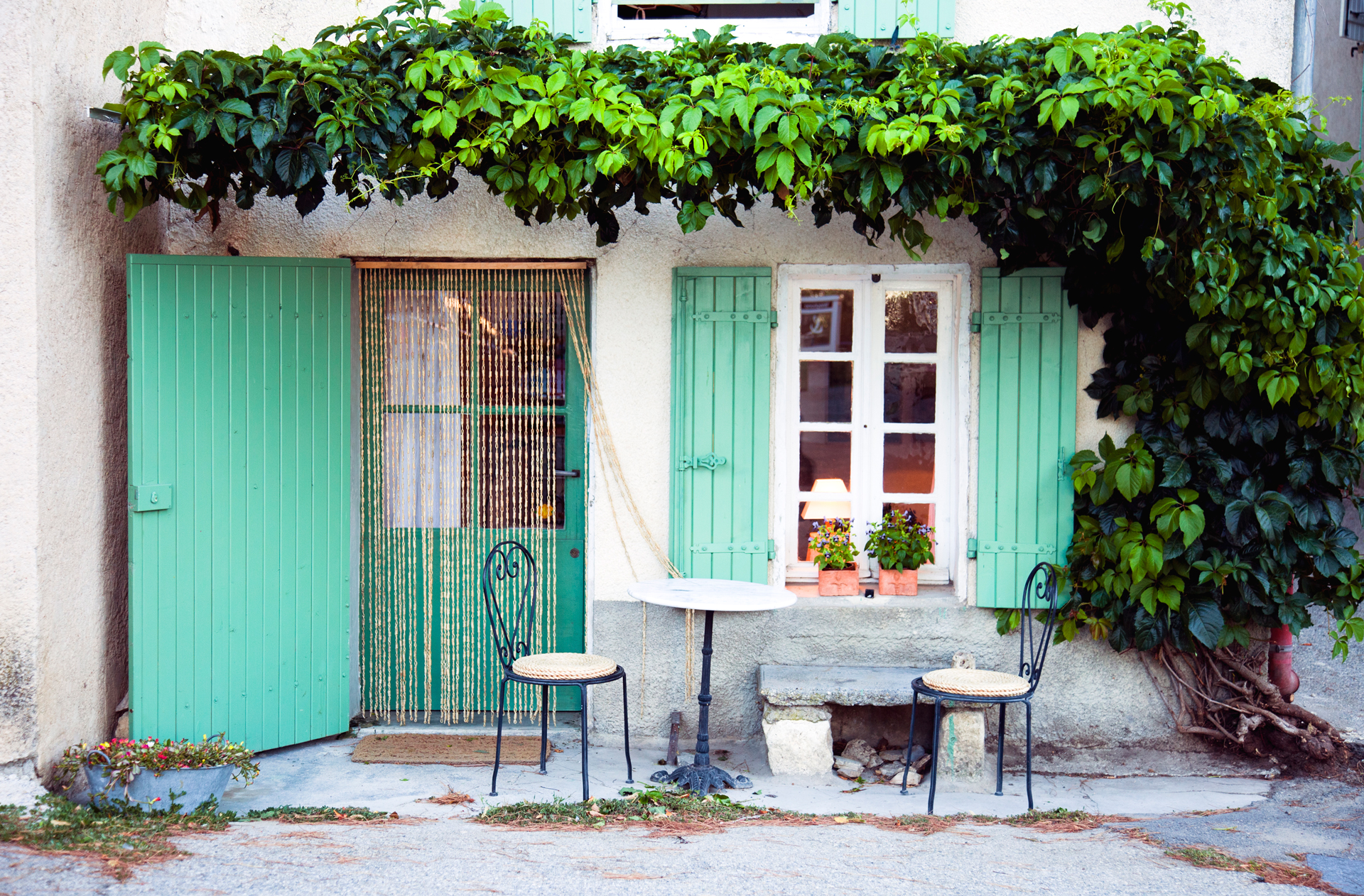 The front of a house in Provence with flowers lining the wall and outdoor seating