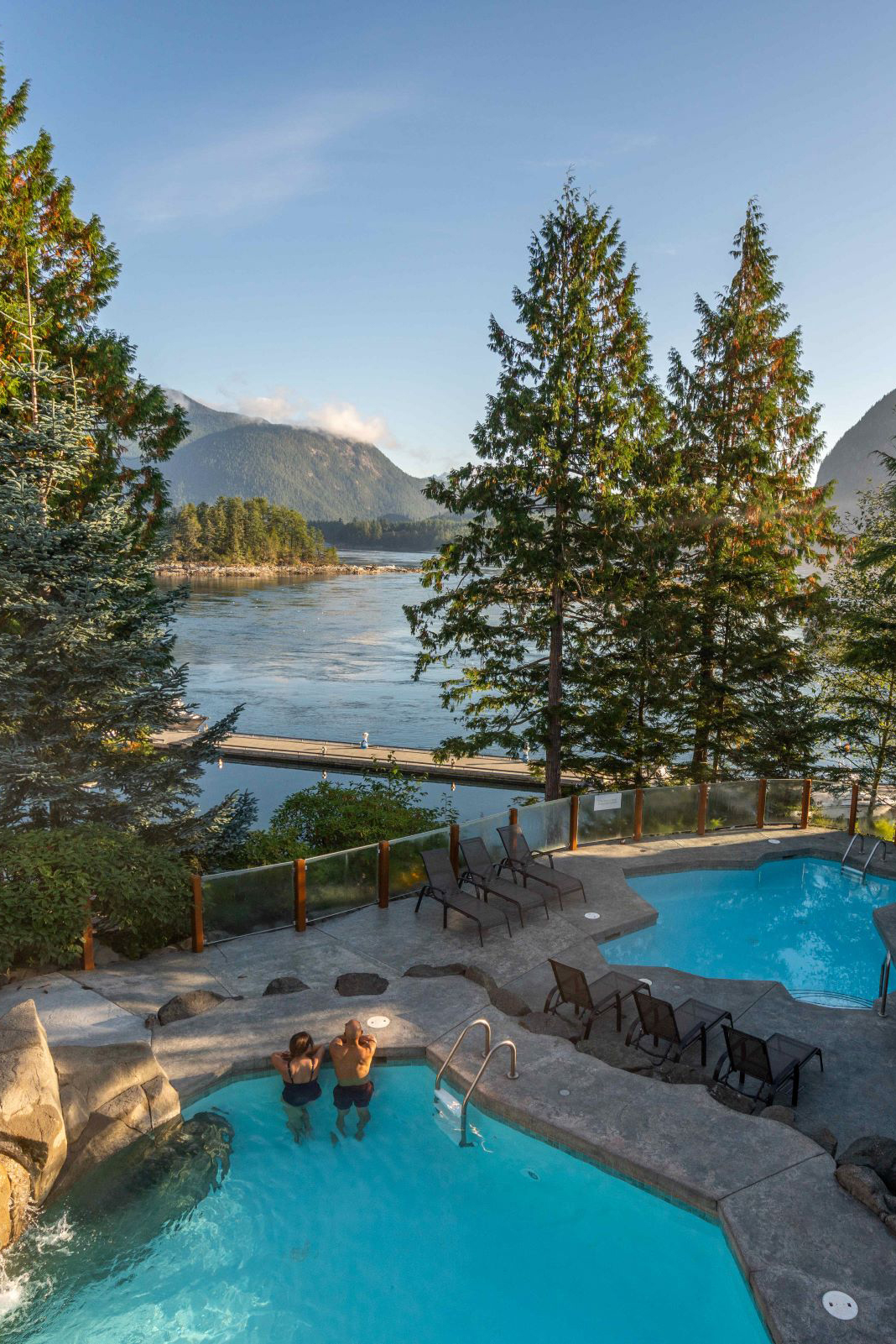 Couple standing in the swimming pool at Sonora Resort looking between two trees out to the vast landscape and lake beyond