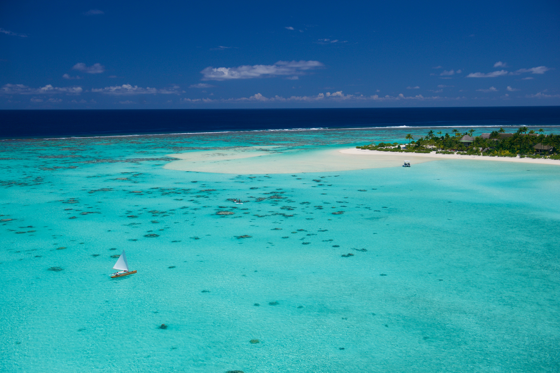 An aerial view of boats on the sea with an island shoreline on the right