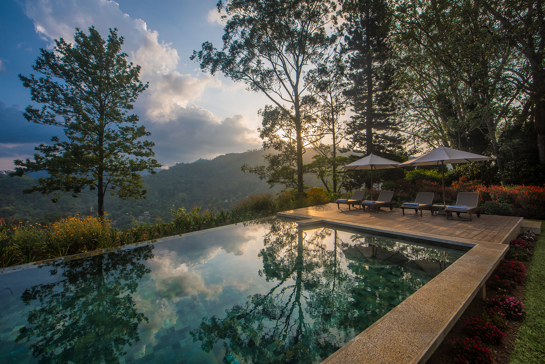 Pool reflecting the sky and clouds flanked by sun loungers and trees