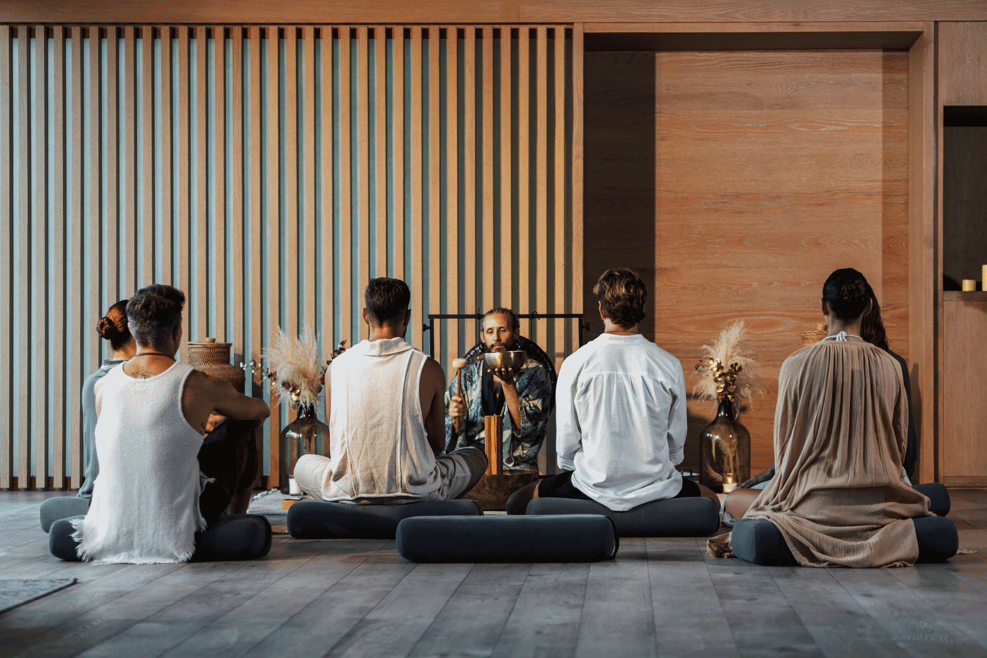 Group seated on cushions in a wellness space during a guided sound healing session with a singing bowl.