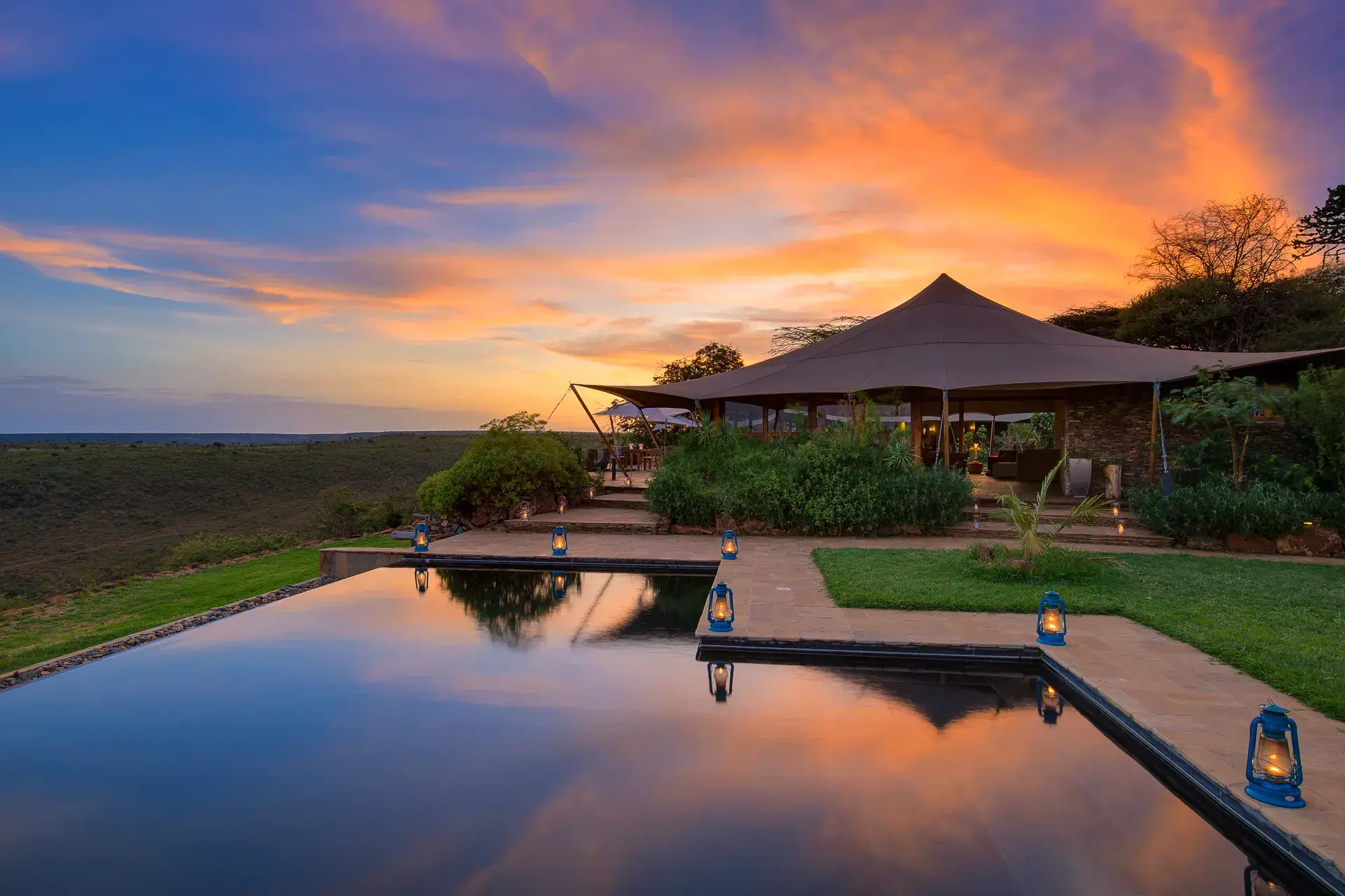 The main infinity pool at Elewana Loisaba Tented Camp featuring lanterns positioned around the edge with a communcal tent behind at sunset