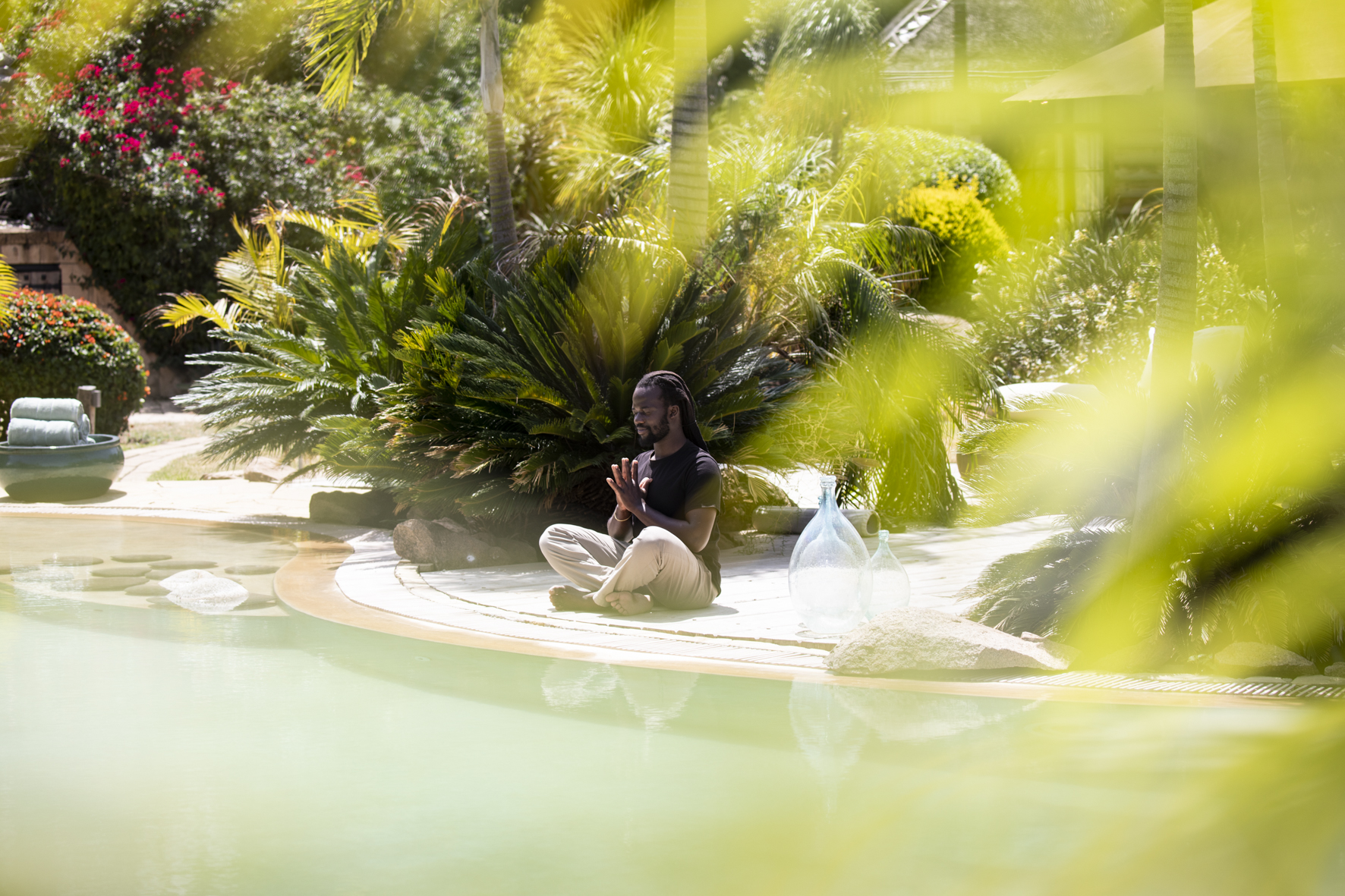 A man practising yoga beside a pool surrounded by ferns and greenery