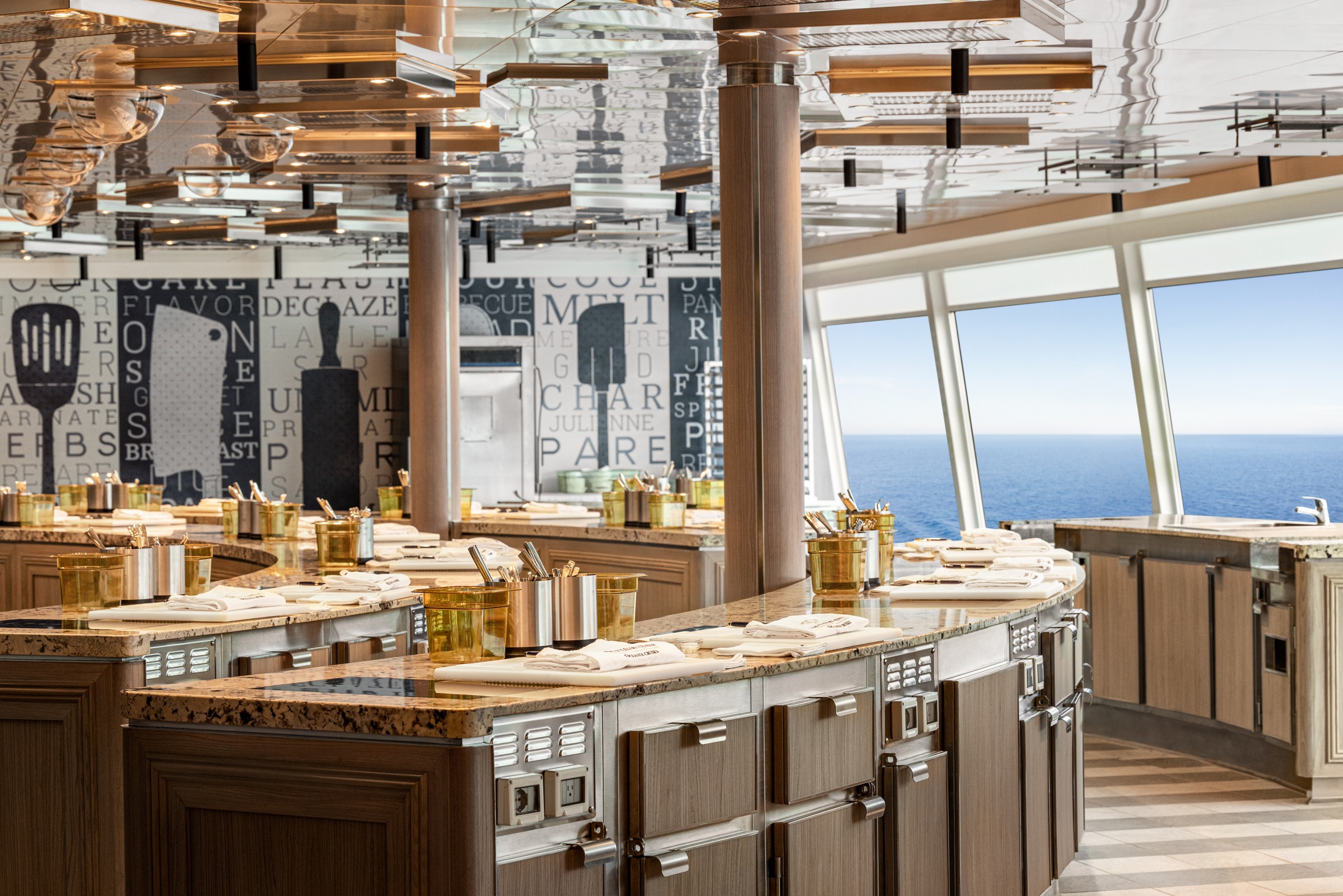 Modern Oceania Cruises culinary centre with cooking stations, stainless steel appliances, and panoramic ocean view.