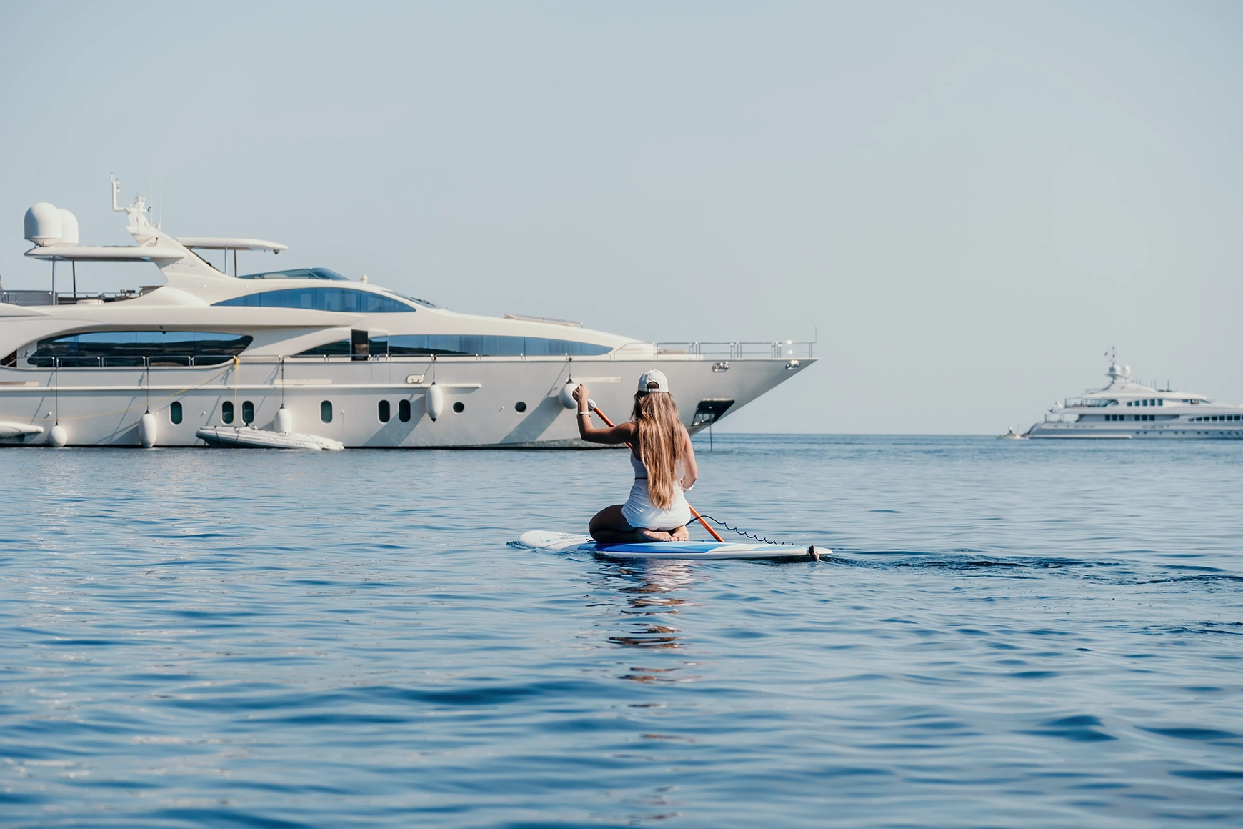 A woman knelt on a paddleboard in front of a luxury private yacht