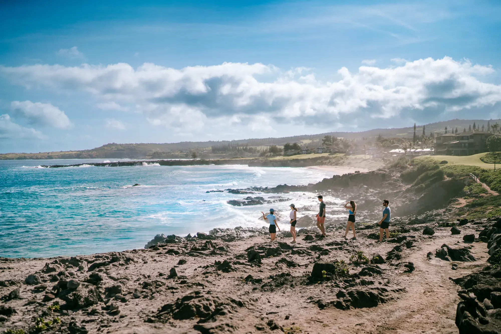 A group of guests at The Ritz-Carlton Maui, Kapalua walking along the rocky headland with the ocean in front beneath a clear sky