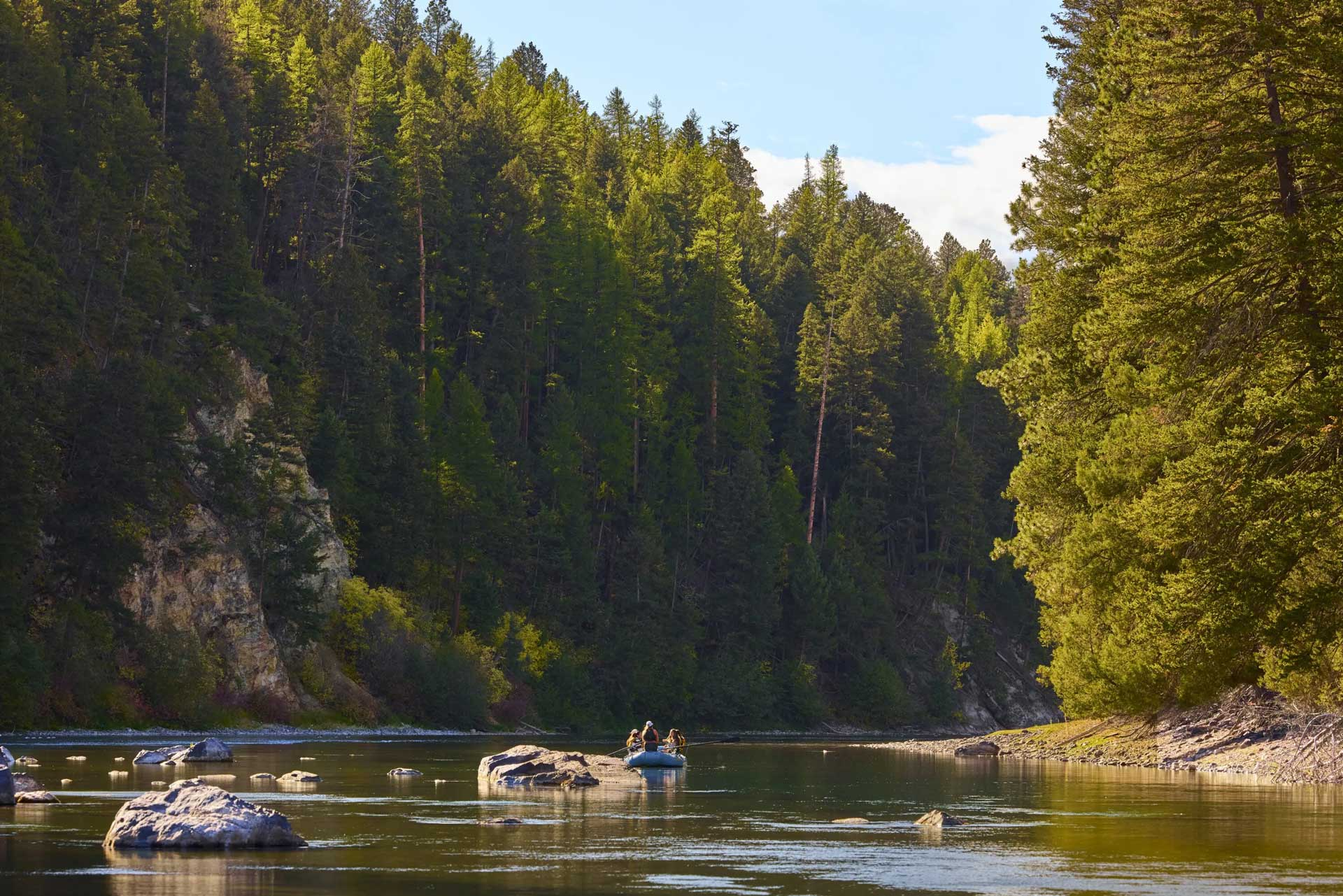 Small group rafting on a calm river surrounded by dense forest and rocky banks in a scenic natural setting.