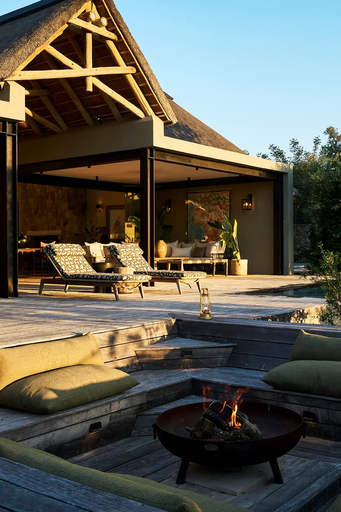 The outside terrace of the villa at Monwana Game Reserve featuring lounge furniture on the deck and a sunken firepit in front of a thatched wooden building 