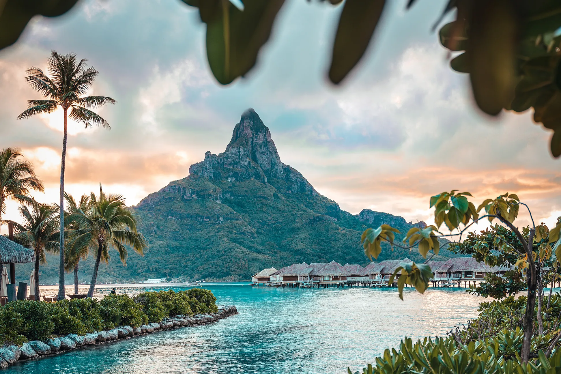 Scenic view of Mount Otemanu in Bora Bora with turquoise lagoon, overwater bungalows, and lush tropical greenery at sunset.