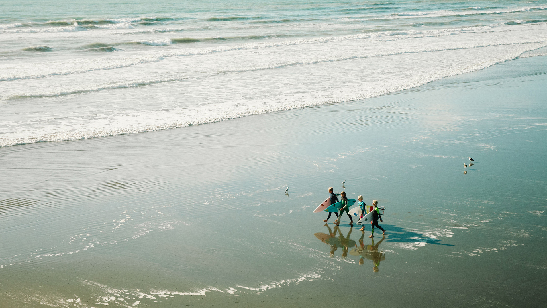 Family of four walking across the beach with surfboards