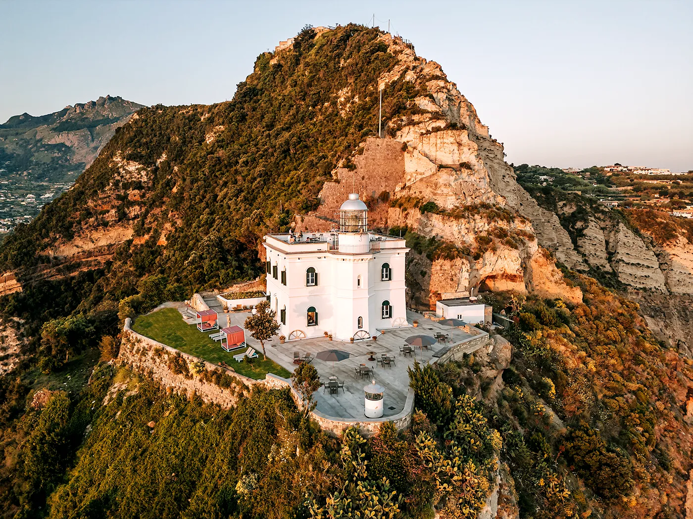 Historic white lighthouse perched on a rocky hilltop surrounded by lush greenery on the Amalfi Coast, Italy.