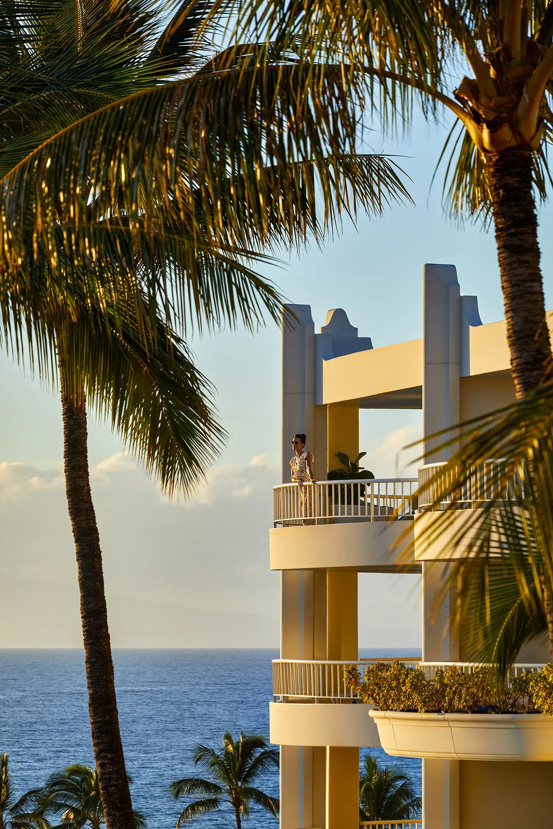 A guest looking out from the balcony of a corner suite at Fairmont Kea Lani with tall palm trees in the foreground and the ocean behind