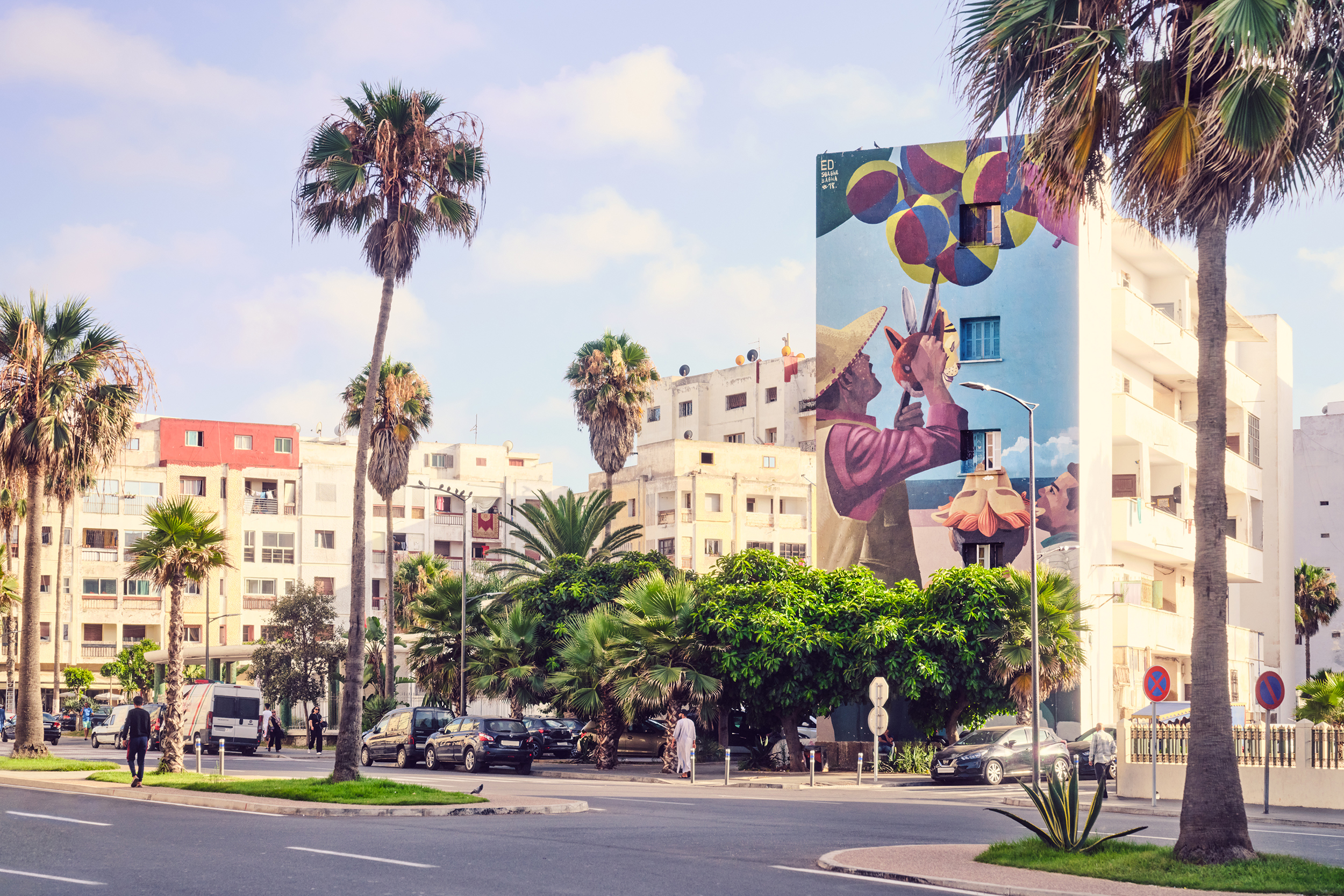 A street in Casablanca lined with palm trees featuirng a large street art mural on the side of a white building