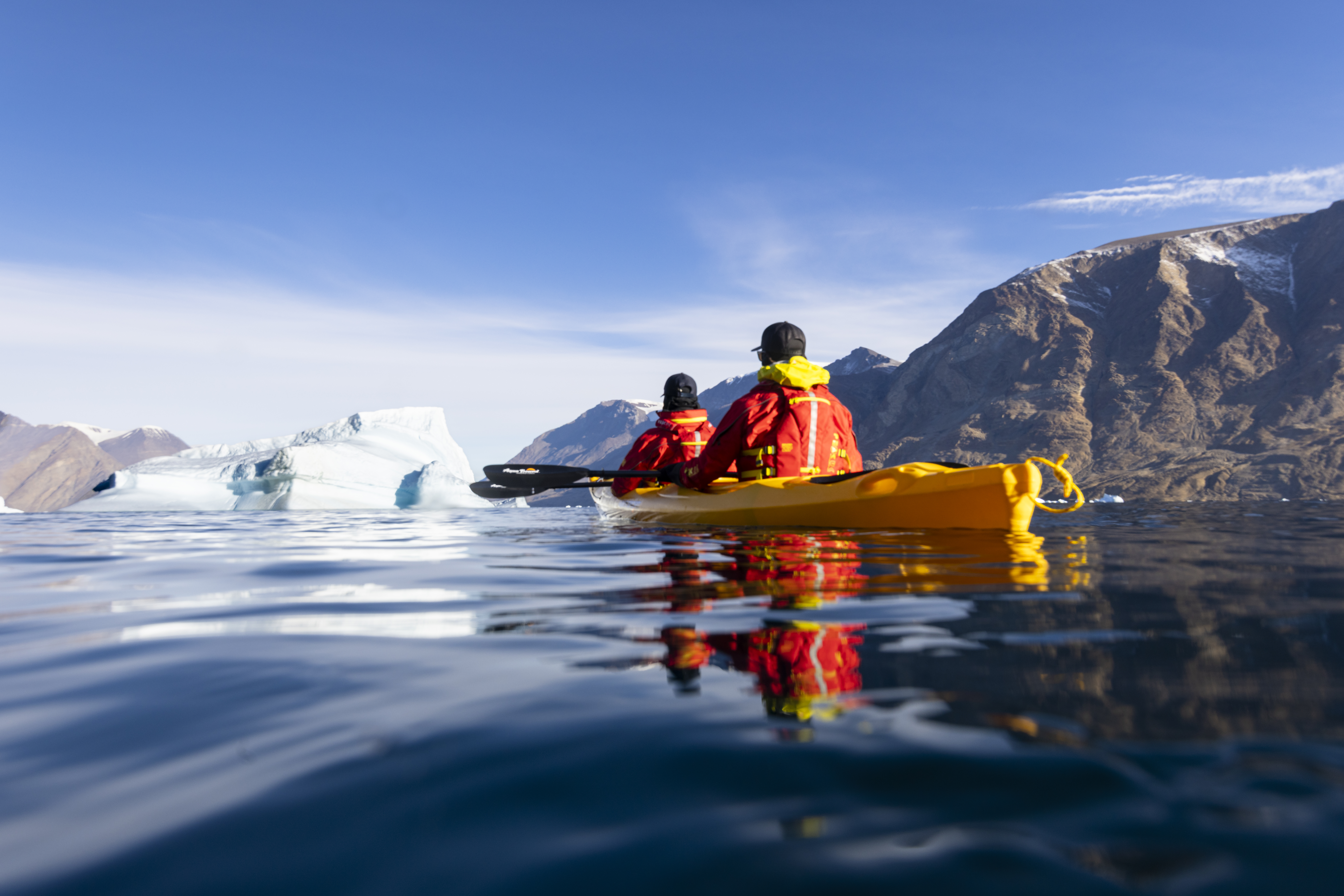 Two people in a yellow kayak paddling among ice bergs in Greenland
