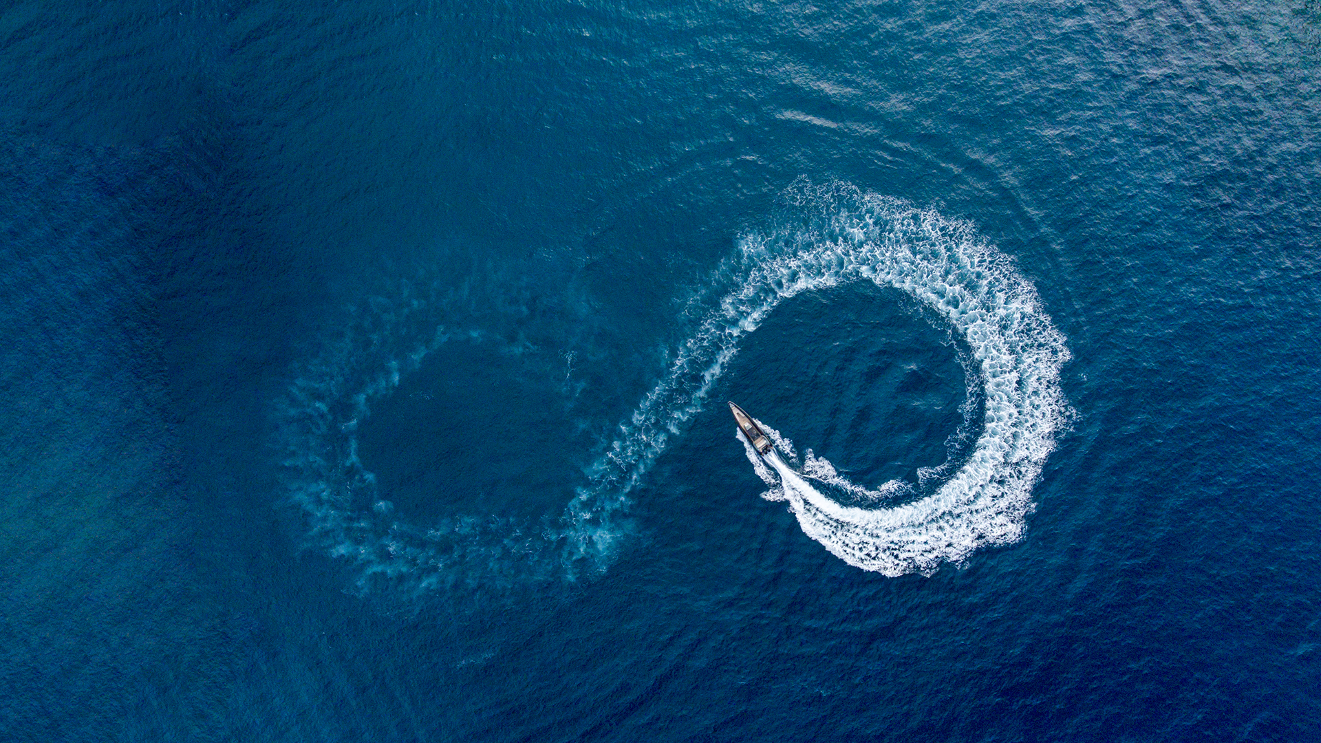 A bird's eye view of a speedboat on azure waters which has created a figure-eight illusion in the waves
