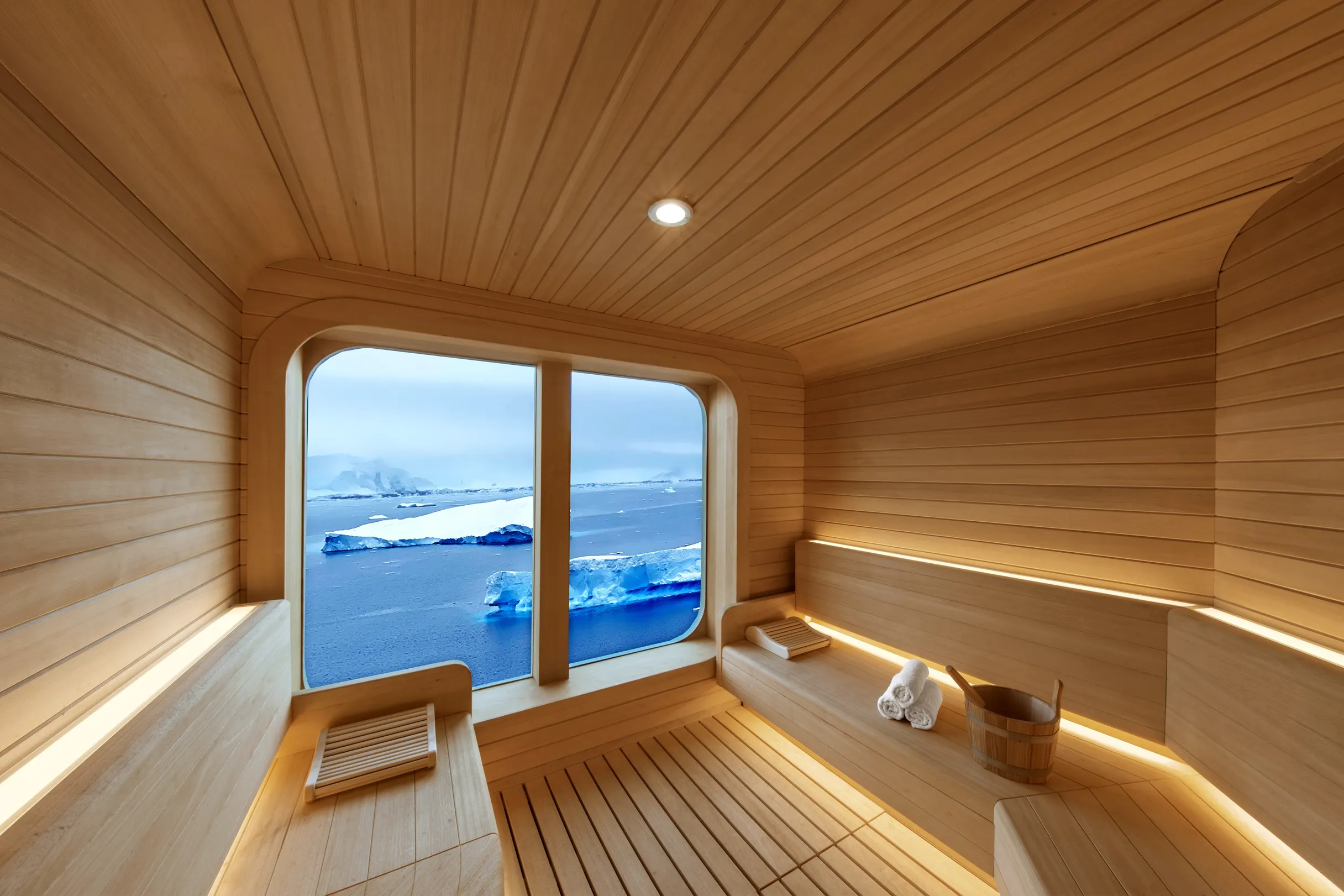 Wooden sauna room with a large window overlooking icebergs in the ocean.