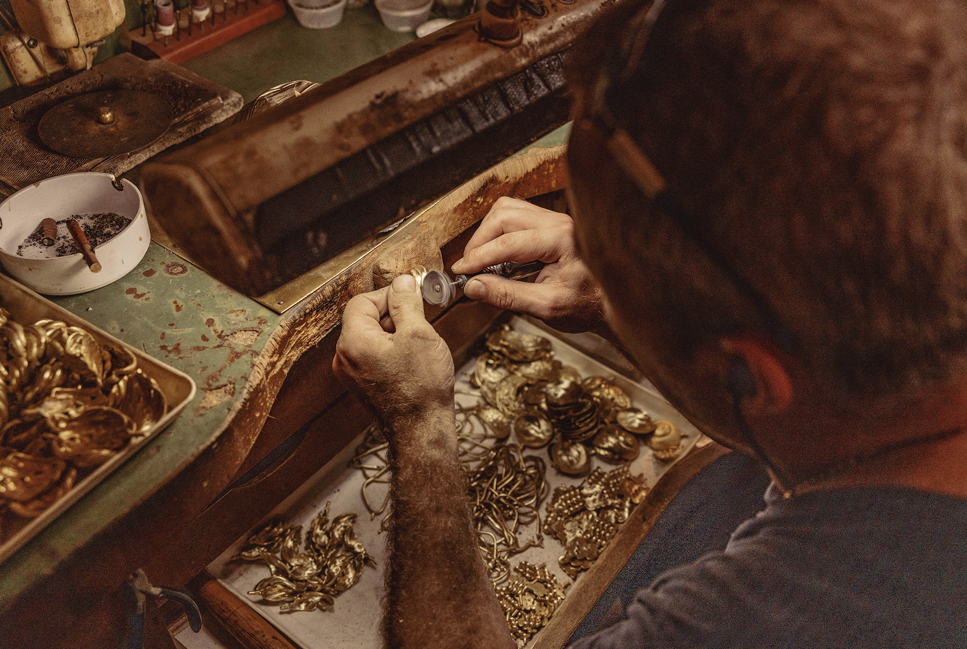 Male jeweller crafting gold pendants on a workbench in his workshop