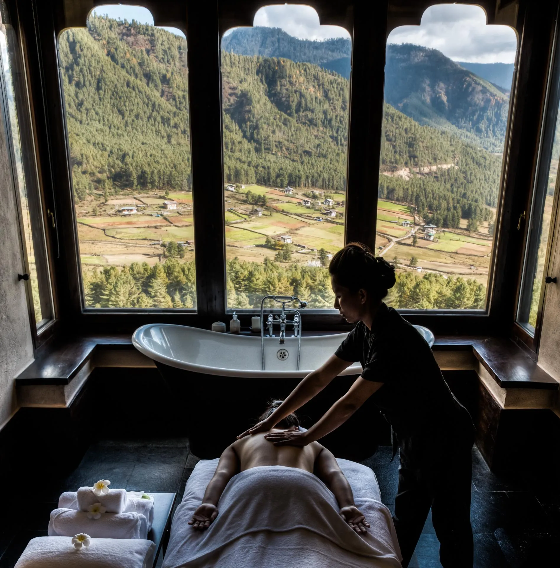 In‑suite massage beside a freestanding bath with panoramic valley and forest views.