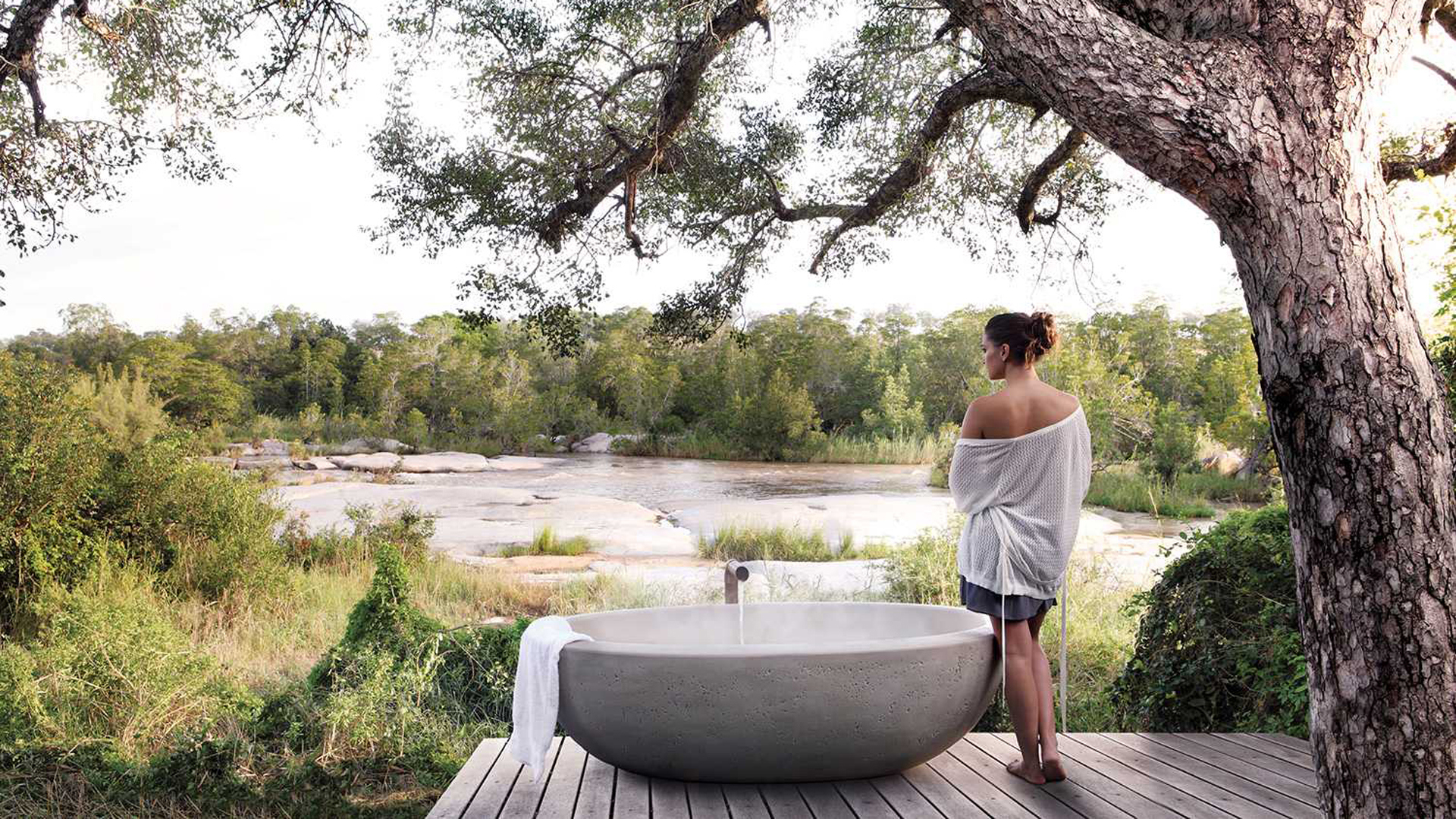A woman stood next to an outdoor bath which is near a river