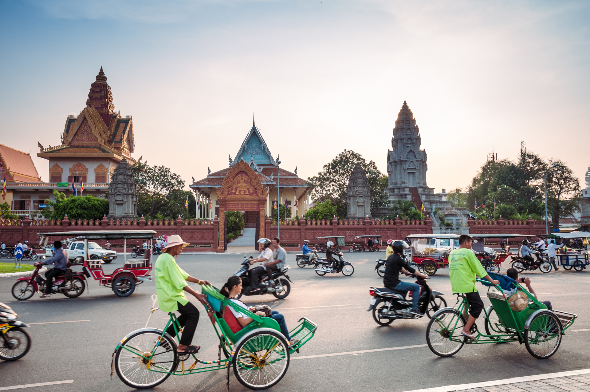 A busy road with bikes and tuktuks in front of a temple