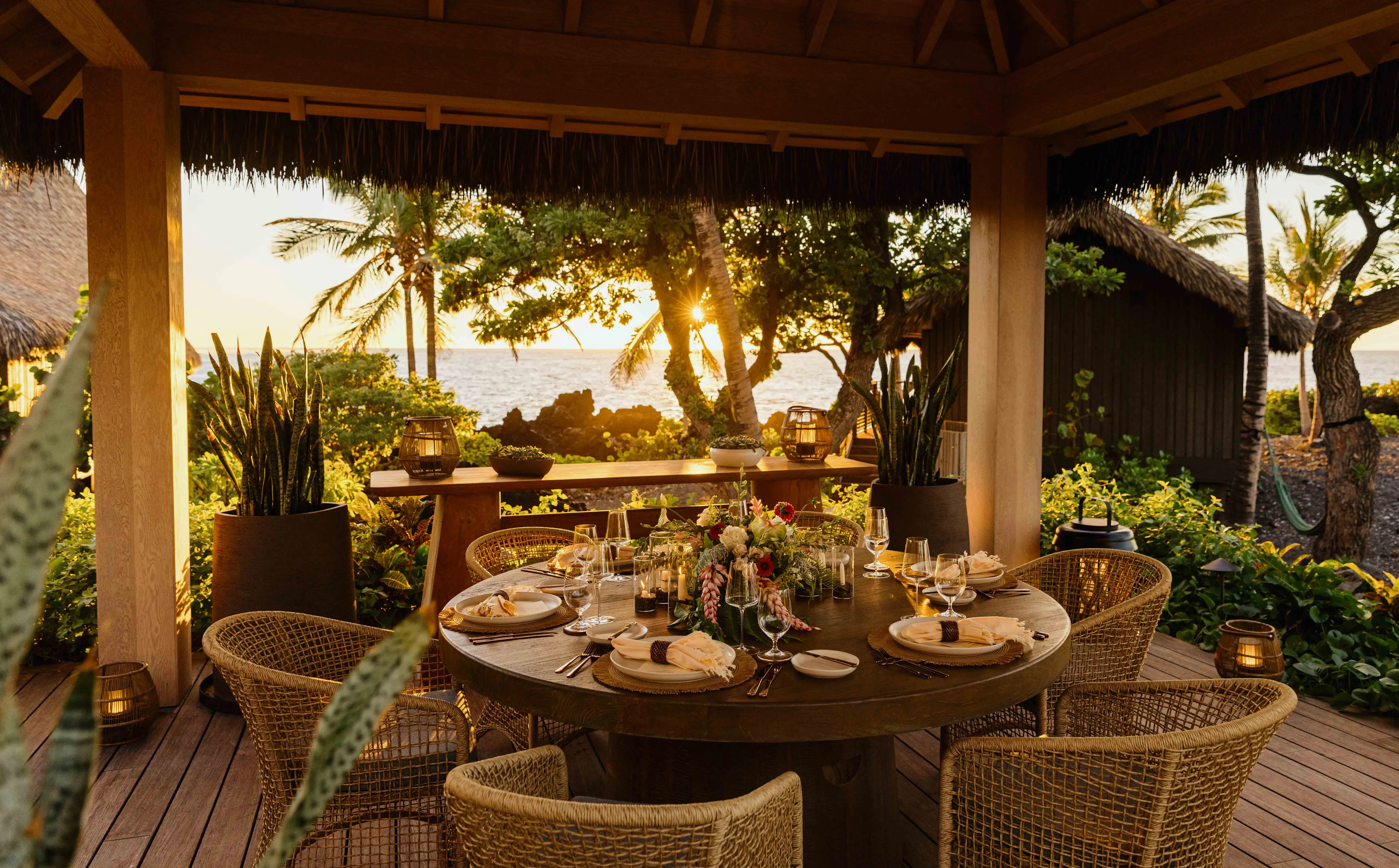 A large round table set for dinner in a pavilion facing gardens and the ocean