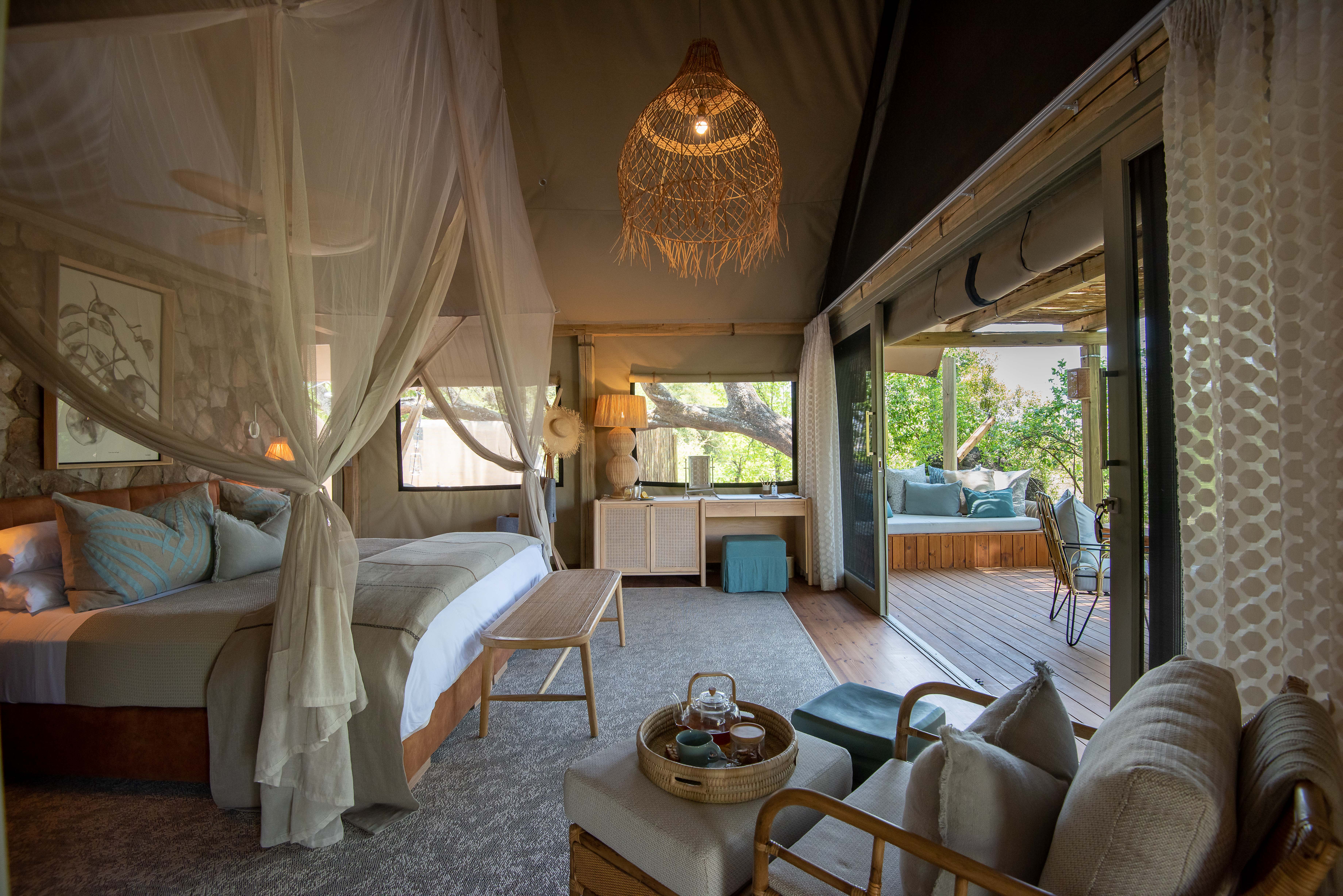 A stylish luxury tent featuring a canopy bed, modern furniture and large sliding doors to a deck outside