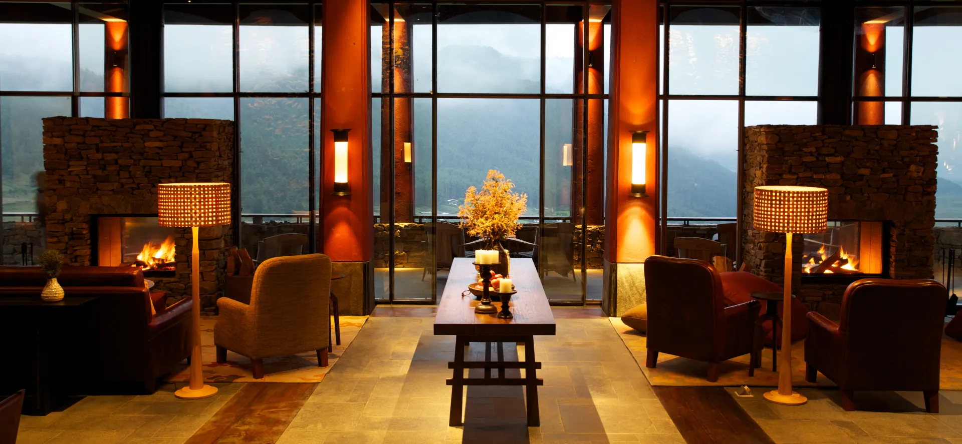 Cosy lounge with sofas and fireplaces framed by large windows overlooking misty mountains.