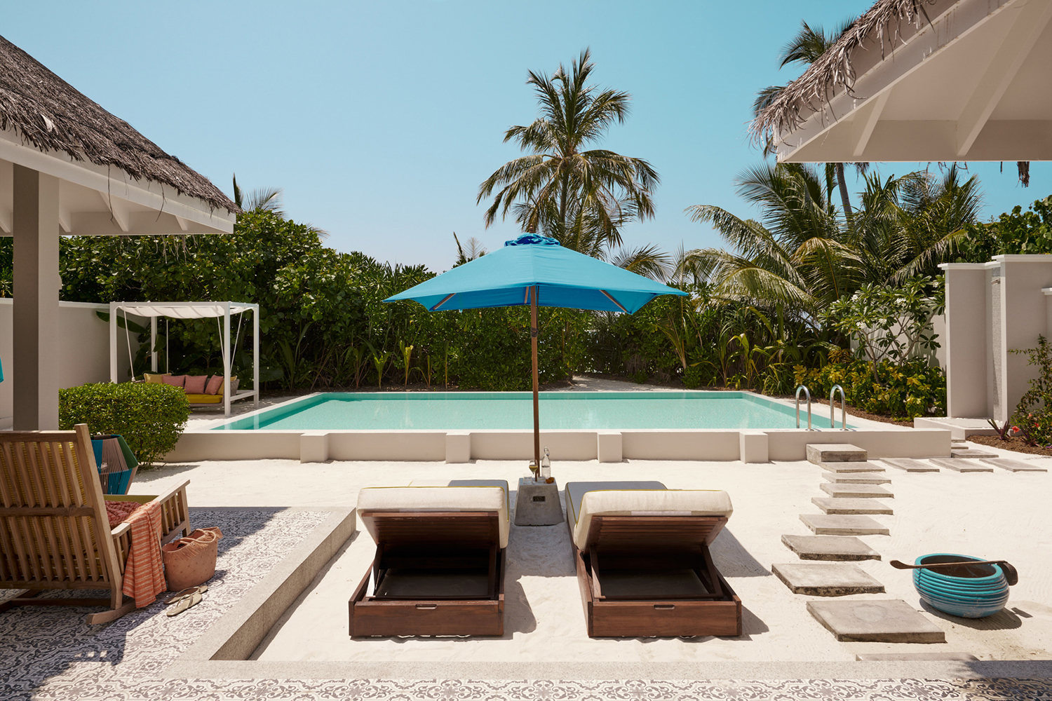 The private pool area of a Beach Villa at Finolhu with sun loungers beneath a blue umbrella and a glimpse of an outdoor shower and cabana with greenery beyond