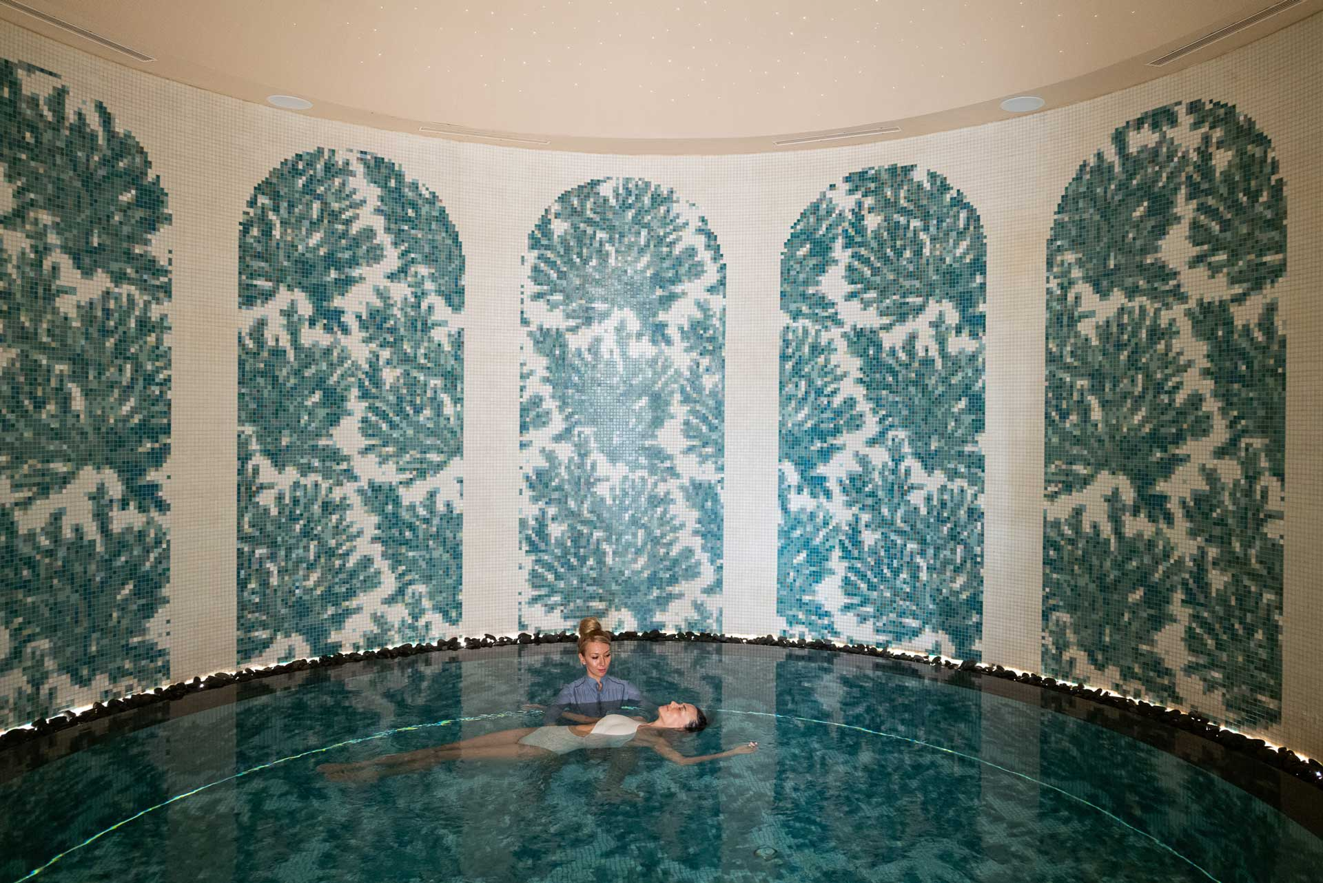 Guest receiving a floating therapy session in a mosaic-lined indoor pool at JOALI BEING.