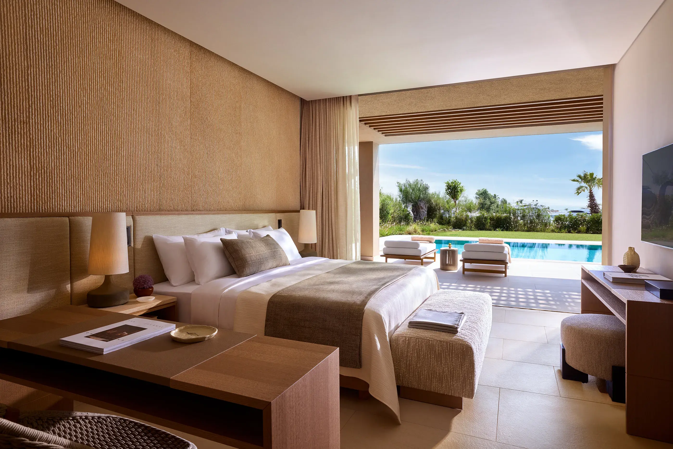 Luxury bedroom in a villa at Sani Asterias in Halkidiki opening onto a private terrace with sun loungers and a serene pool surrounded by lush gardens.