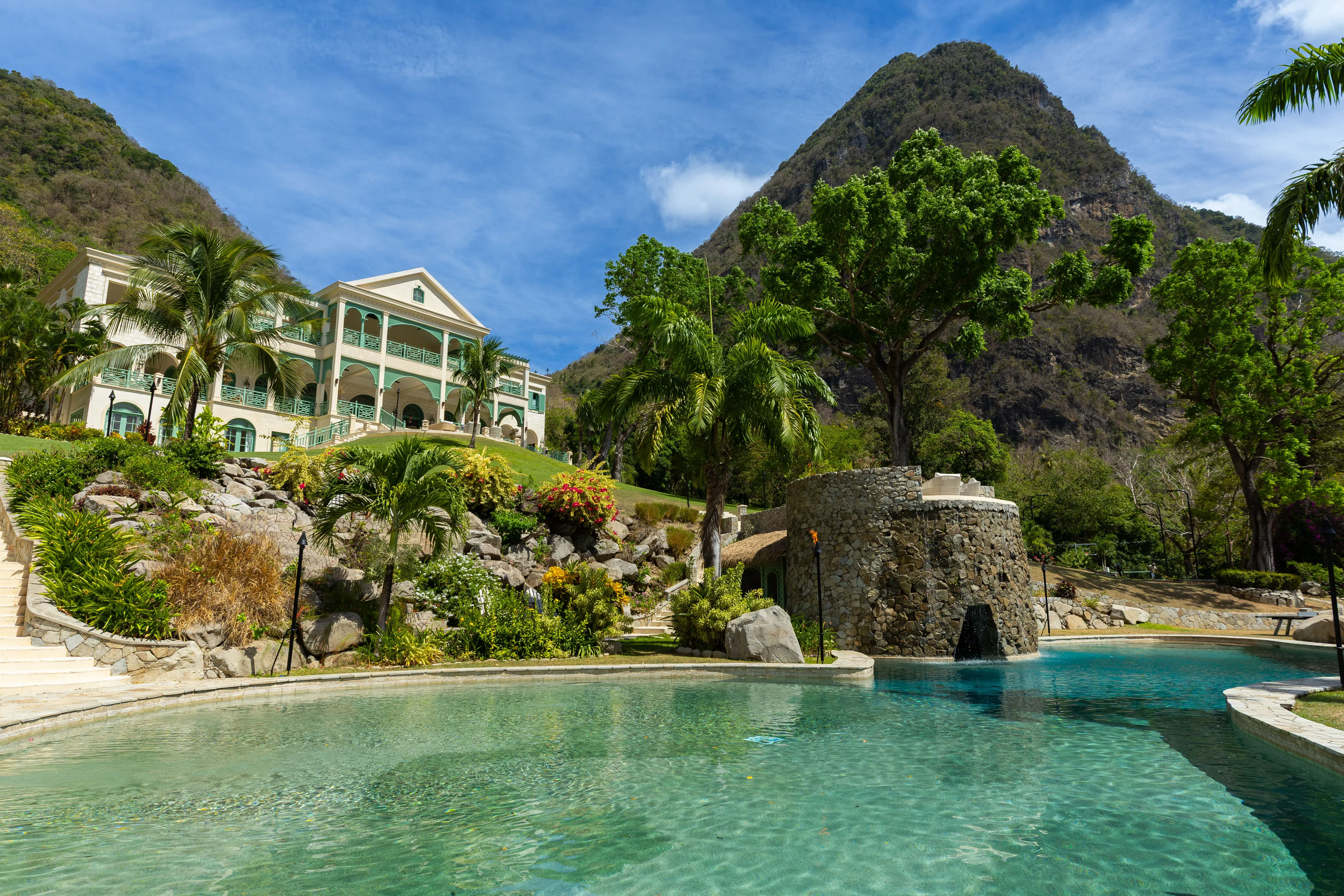 Lagoon-style pool surrounded by tropical gardens with La Belle Helene luxury villa and Piton mountain in the background in St Lucia.