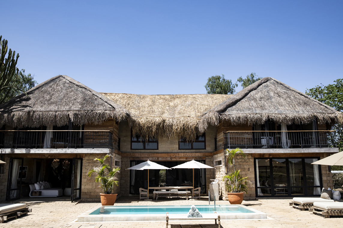 The exterior of a large thatchd villa featuriing balconies and a pool with sun loungers