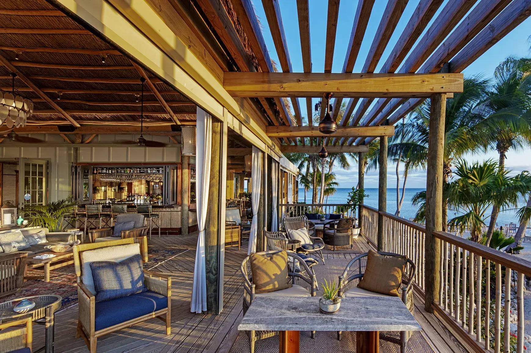 Open-air lounge and bar of Monkey Hut with ocean views at Little Palm Island Resort in Florida, featuring tropical decor and wooden pergola.