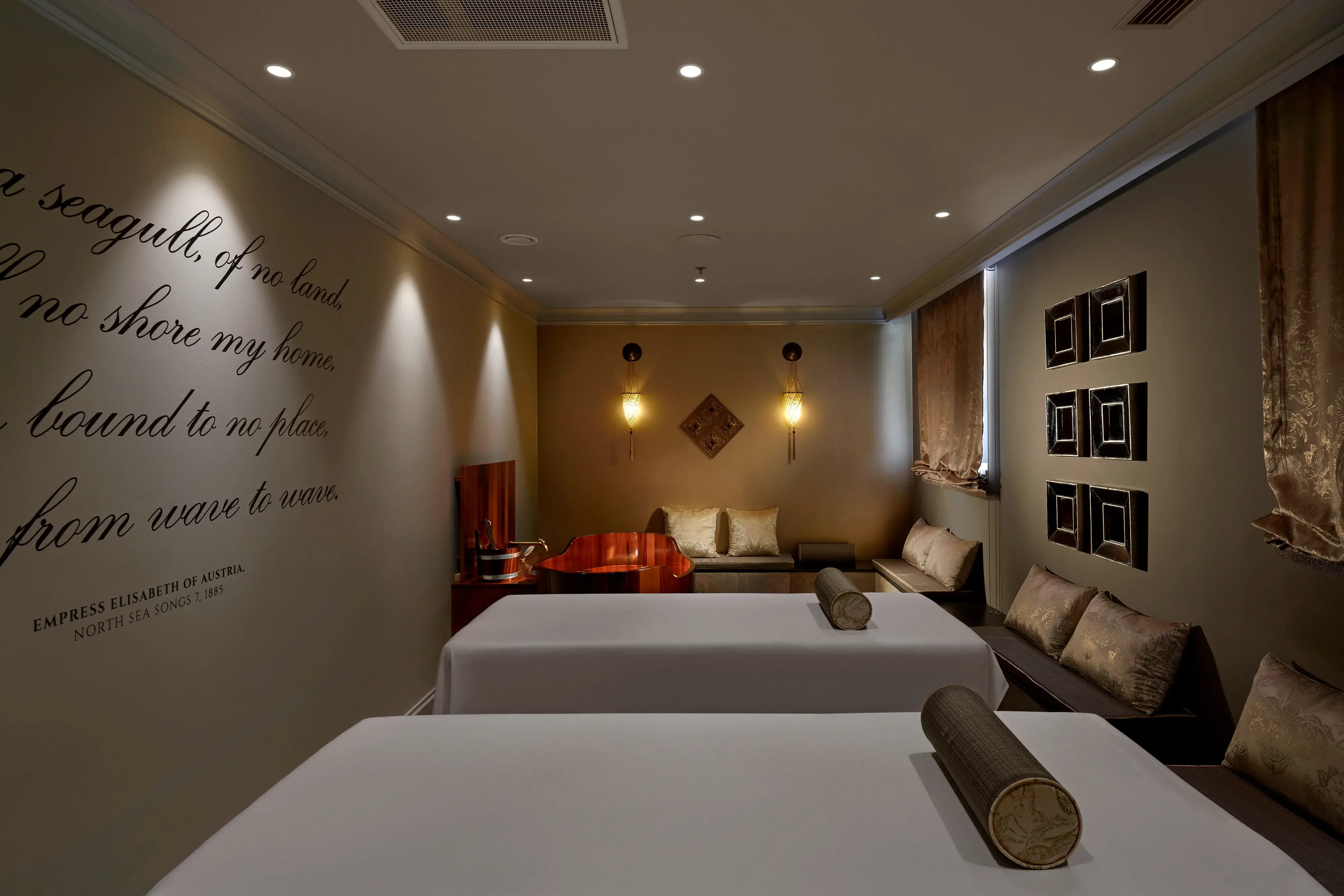 A double spa treatment room at Palace Elisabeth in Croatia featuring two beds and a seating area in low light with pictures and a quote on the walls