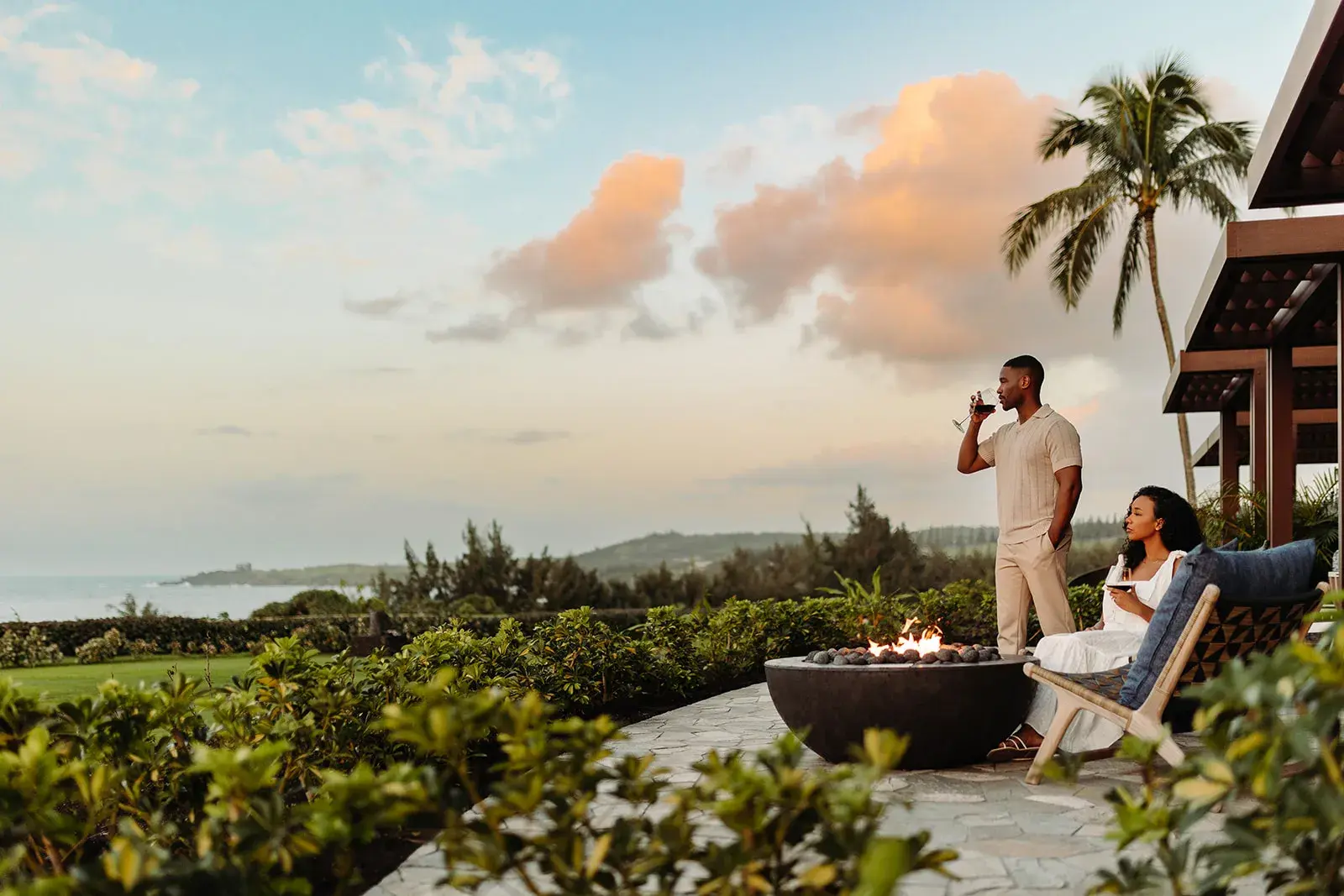 A stylish couple gathered around a fire pit on the terrace of a Fire Lanai Suite at Ritz-Carlton Maui, Kapalua looking out towards the sea
